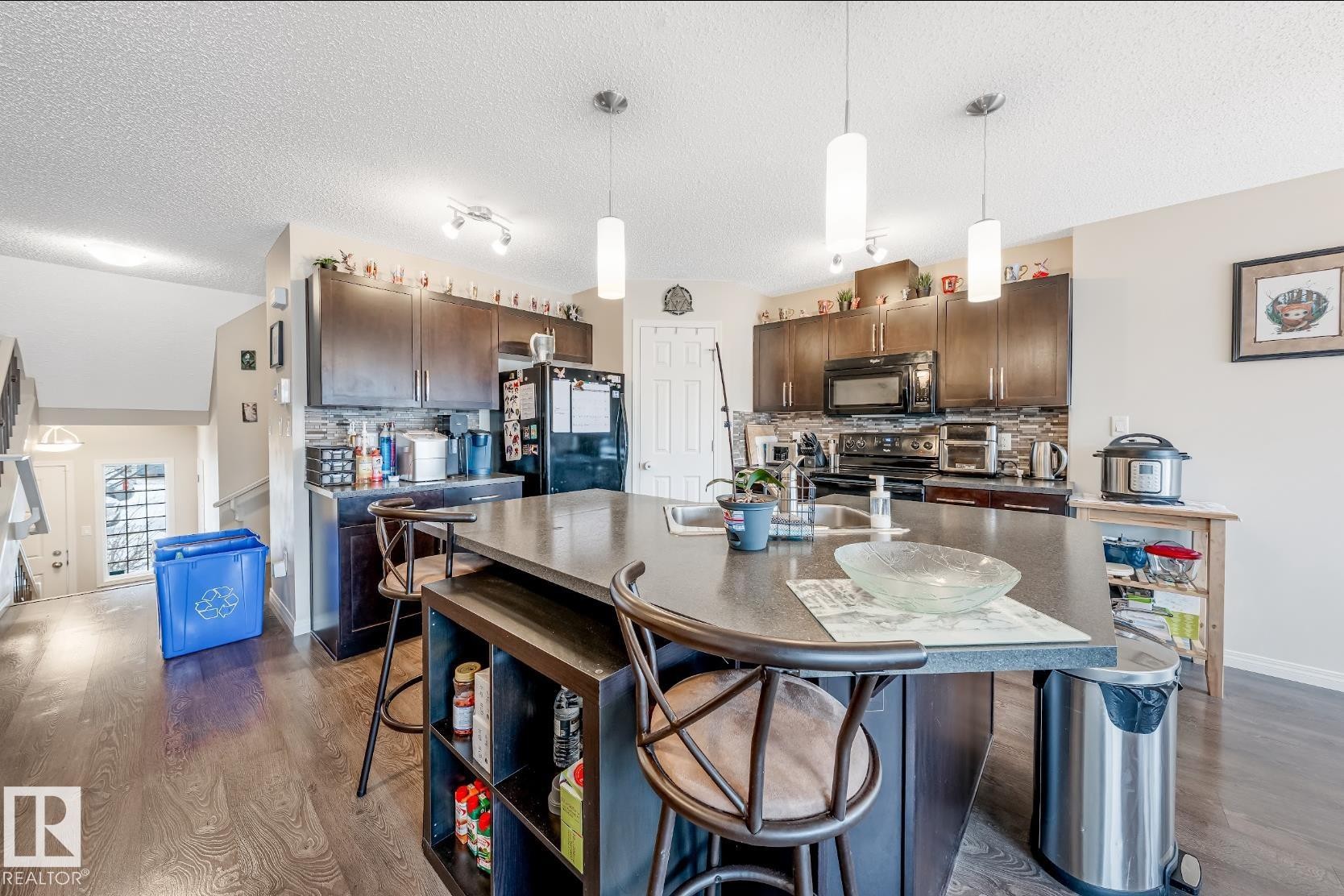 The kitchen features dark wood cabinetry, a dark countertop on the island, and pendant lighting - 3109 Carpenter Landing, Edmonton, AB - Indoor