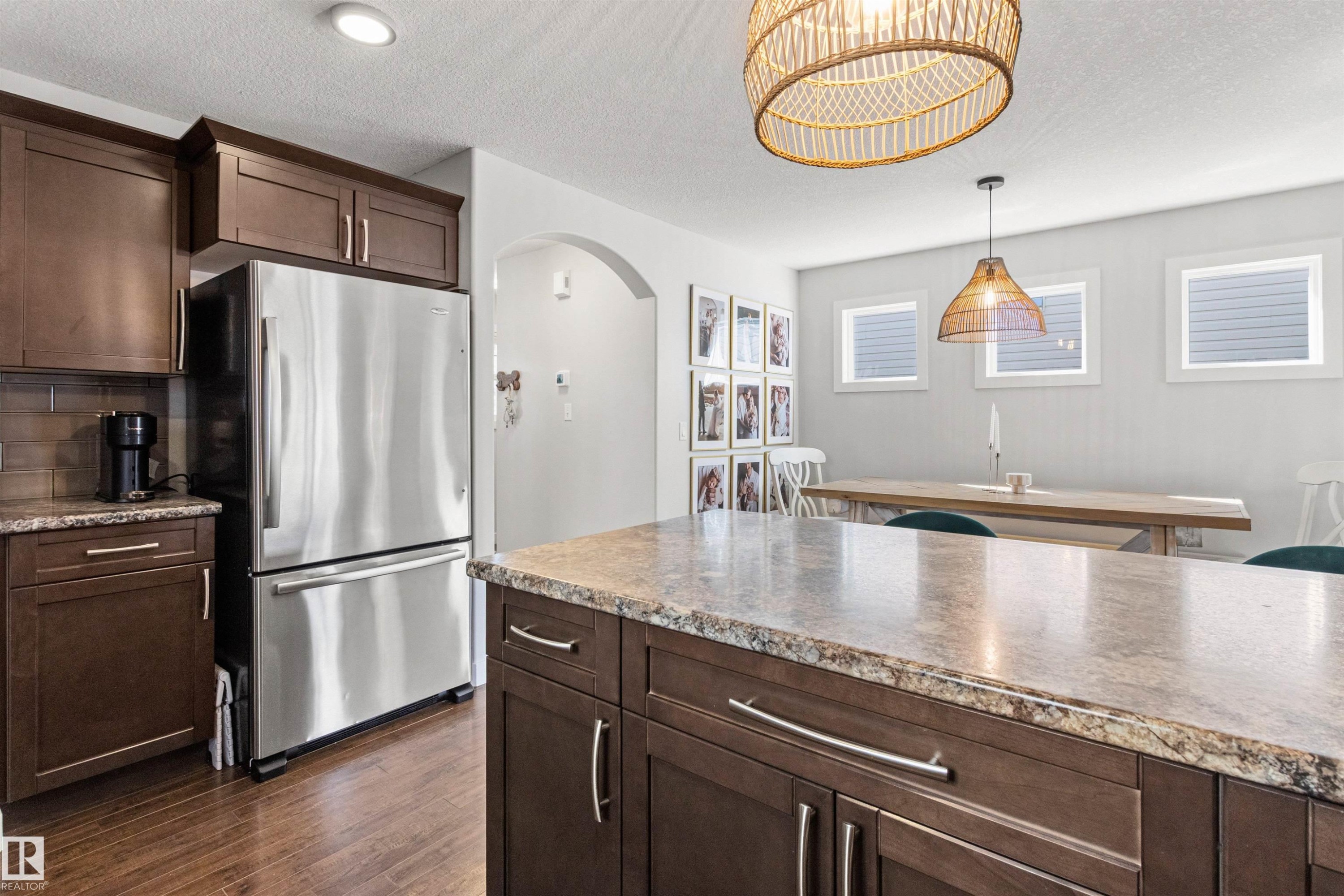 The kitchen features dark wood cabinetry, a stainless steel refrigerator, and a kitchen island with a granite countertop - 38 Hewitt Circle, Spruce Grove, AB - Indoor Photo Showing Kitchen