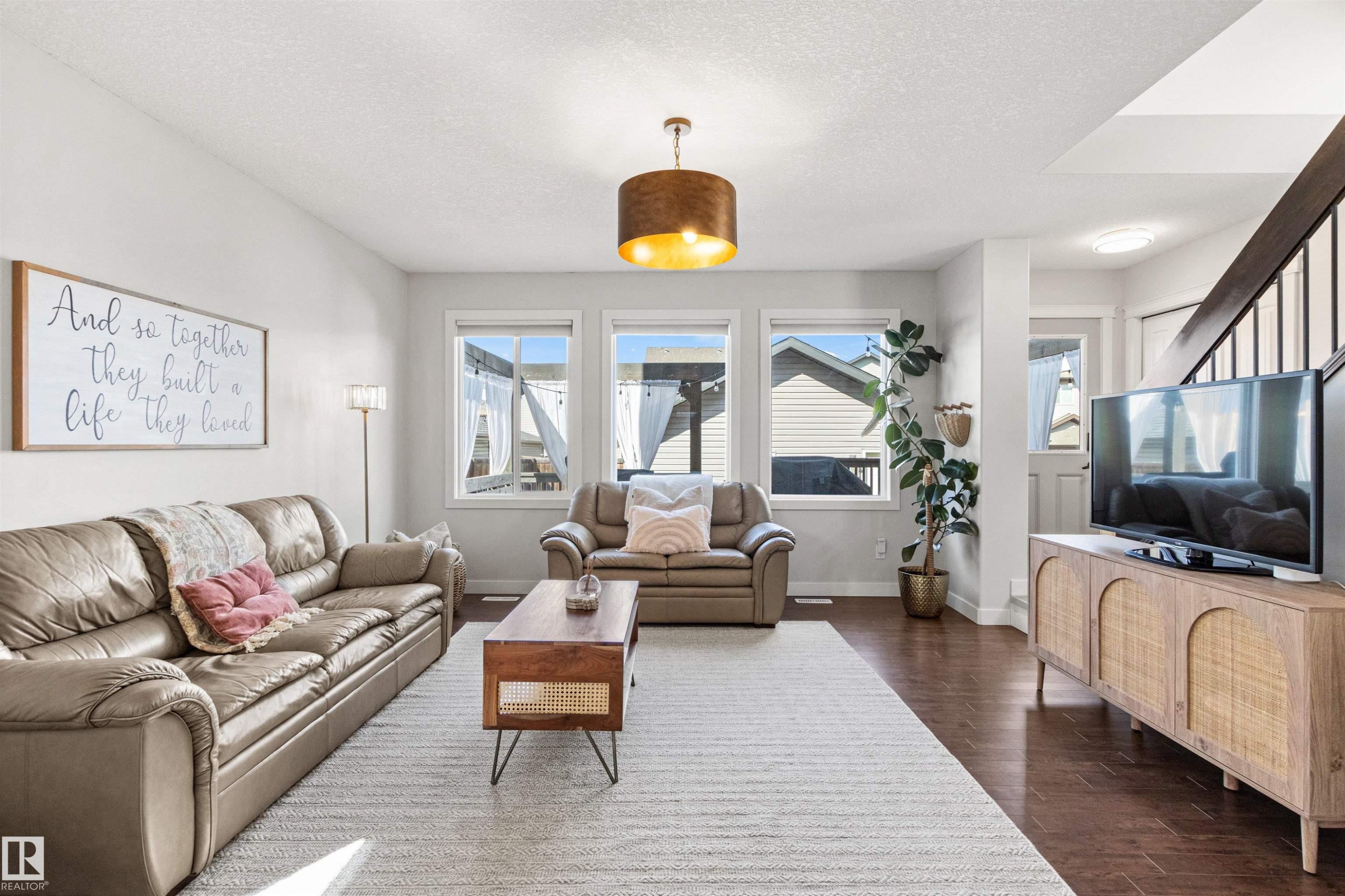 This living area features rich hardwood flooring, light-colored walls, and a contemporary ceiling light fixture - 38 Hewitt Circle, Spruce Grove, AB - Indoor Photo Showing Living Room
