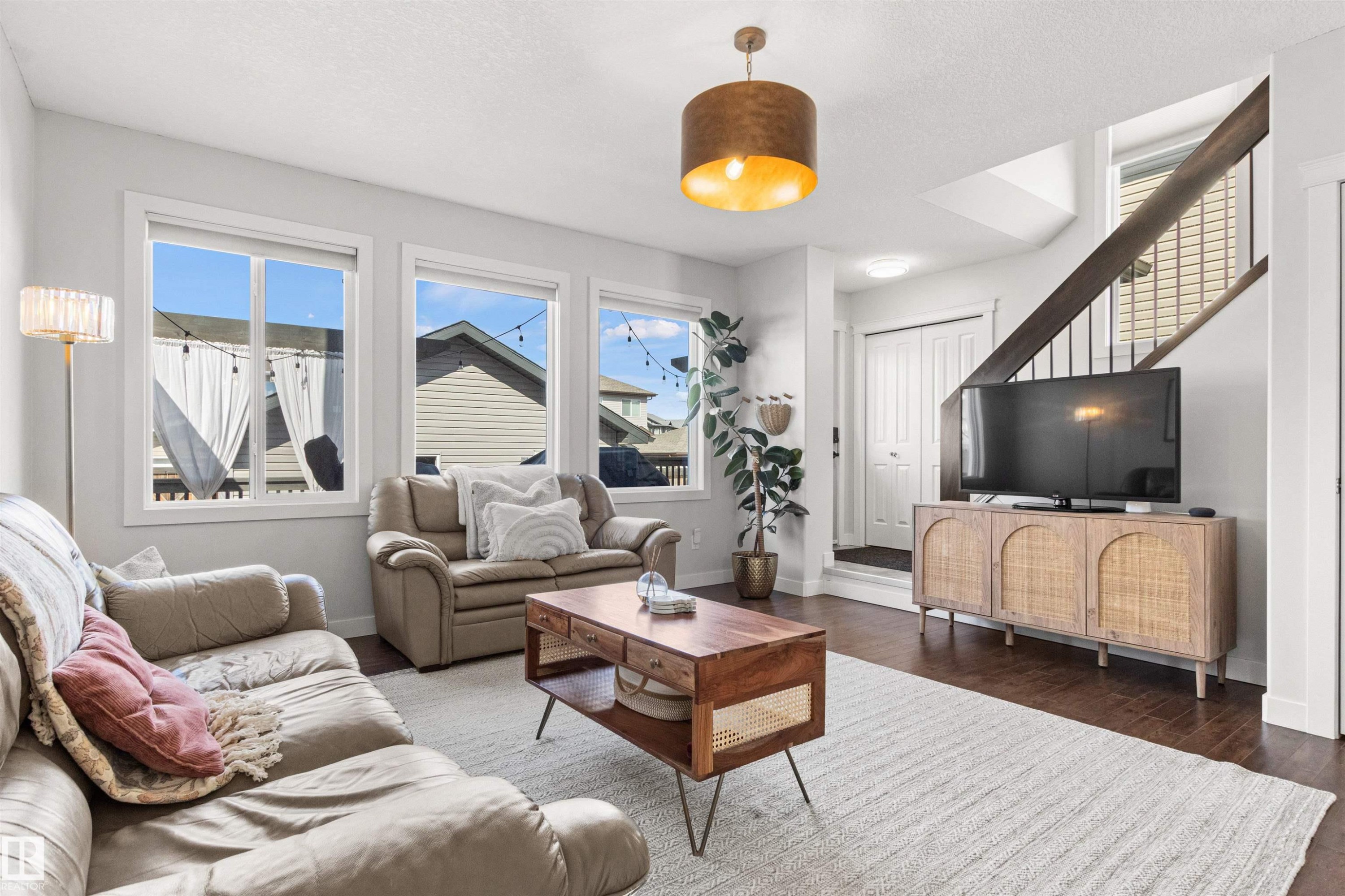 The living area features hardwood flooring, a staircase with dark banisters, and a contemporary light fixture - 38 Hewitt Circle, Spruce Grove, AB - Indoor Photo Showing Living Room