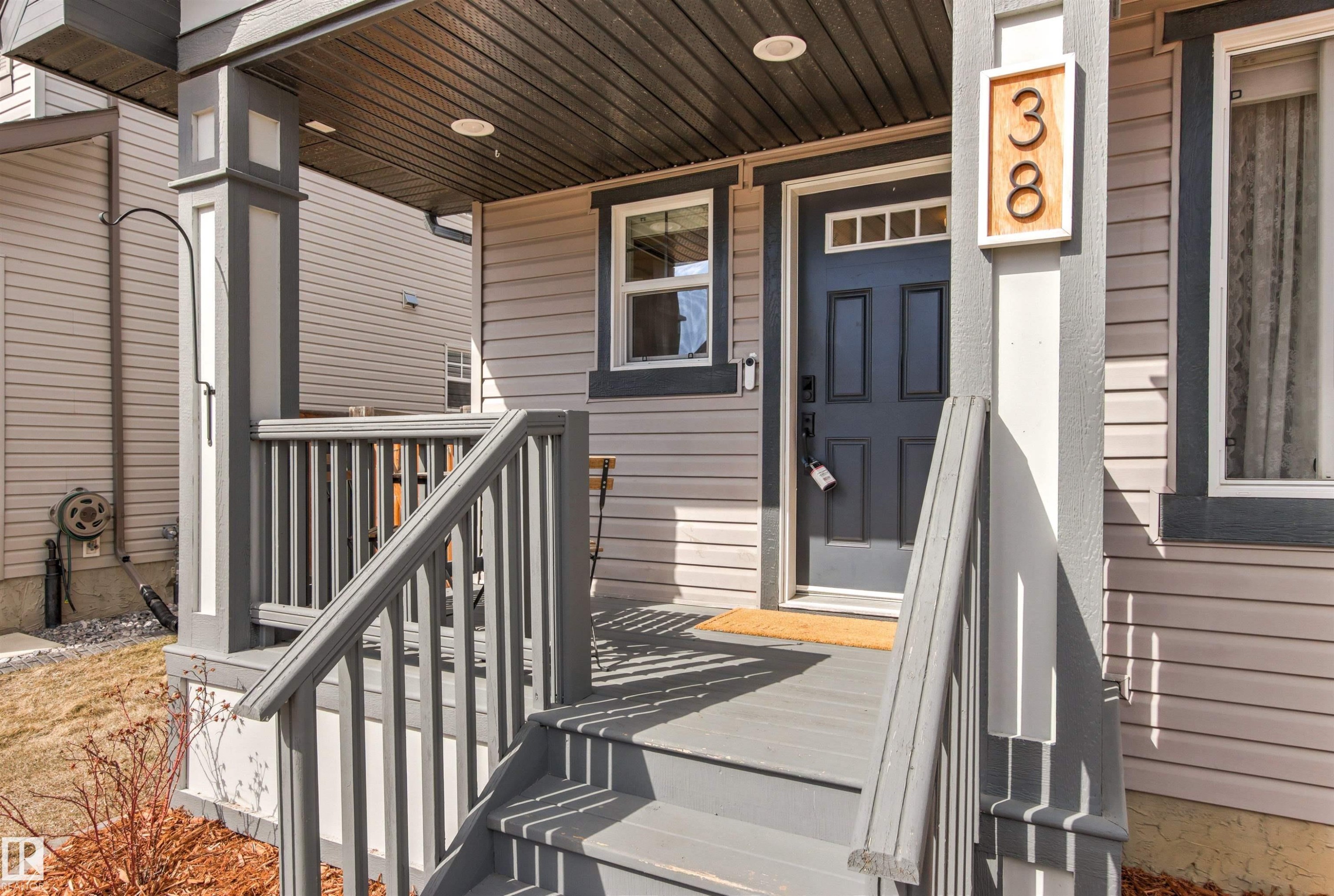 Welcoming front porch with gray steps and railings, featuring a dark paneled door with transom windows - 38 Hewitt Circle, Spruce Grove, AB - Outdoor With Deck Patio Veranda With Exterior