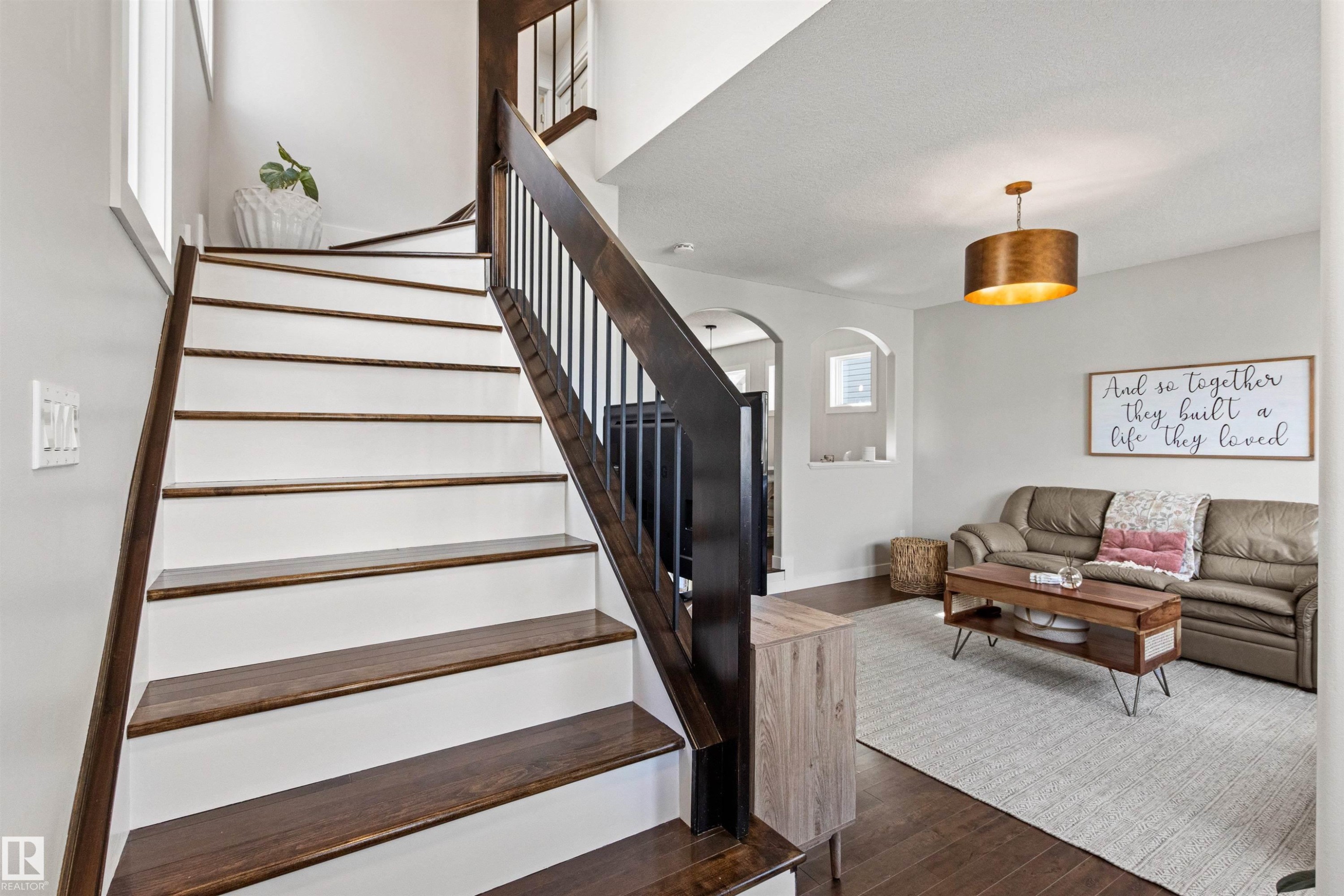 Inviting living area featuring hardwood floors, a staircase with dark wood treads and a white risers, and a contemporary light fixture - 38 Hewitt Circle, Spruce Grove, AB - Indoor Photo Showing Other Room