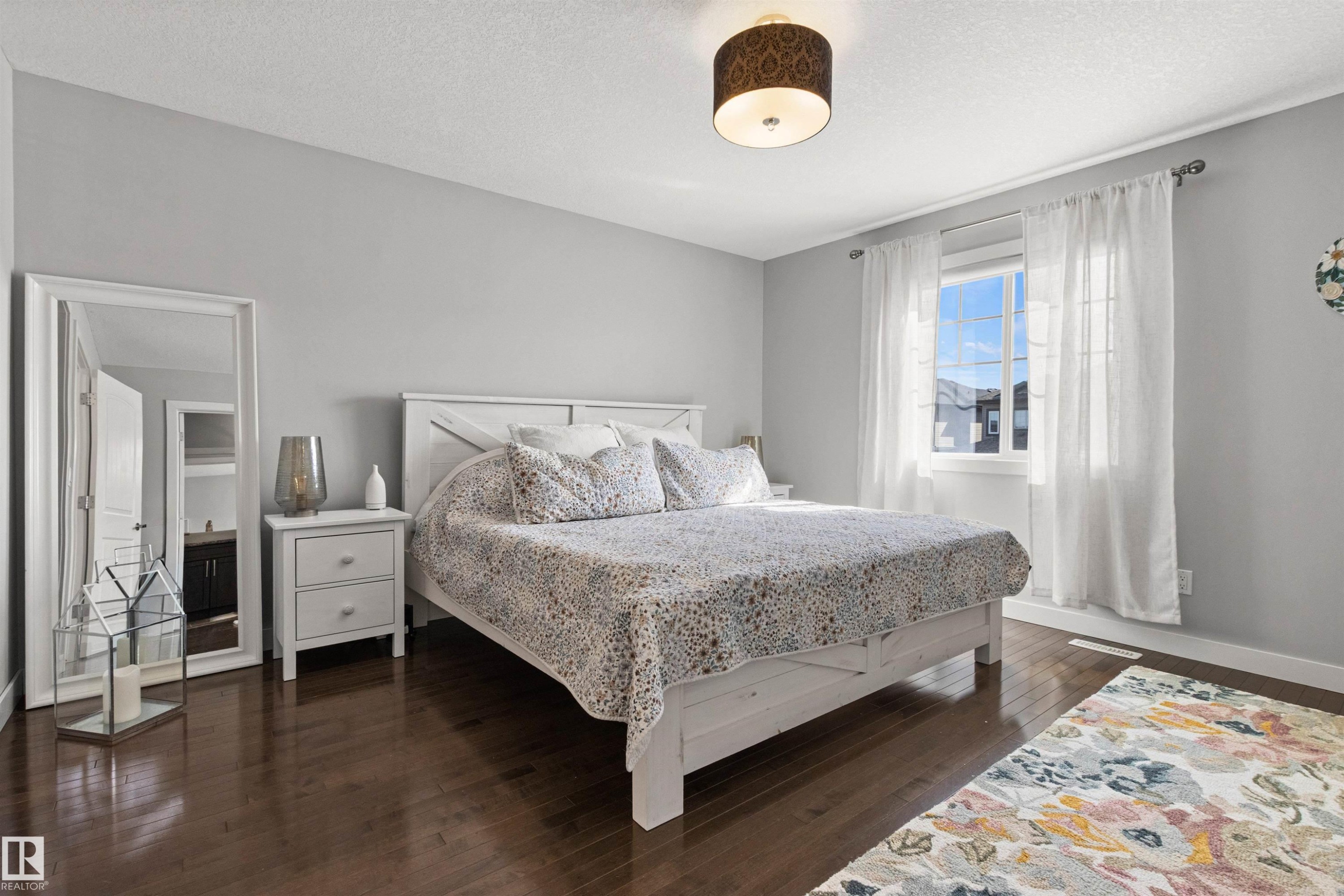 This room features hardwood floors, a large window providing natural light, and a ceiling light fixture - 38 Hewitt Circle, Spruce Grove, AB - Indoor Photo Showing Bedroom