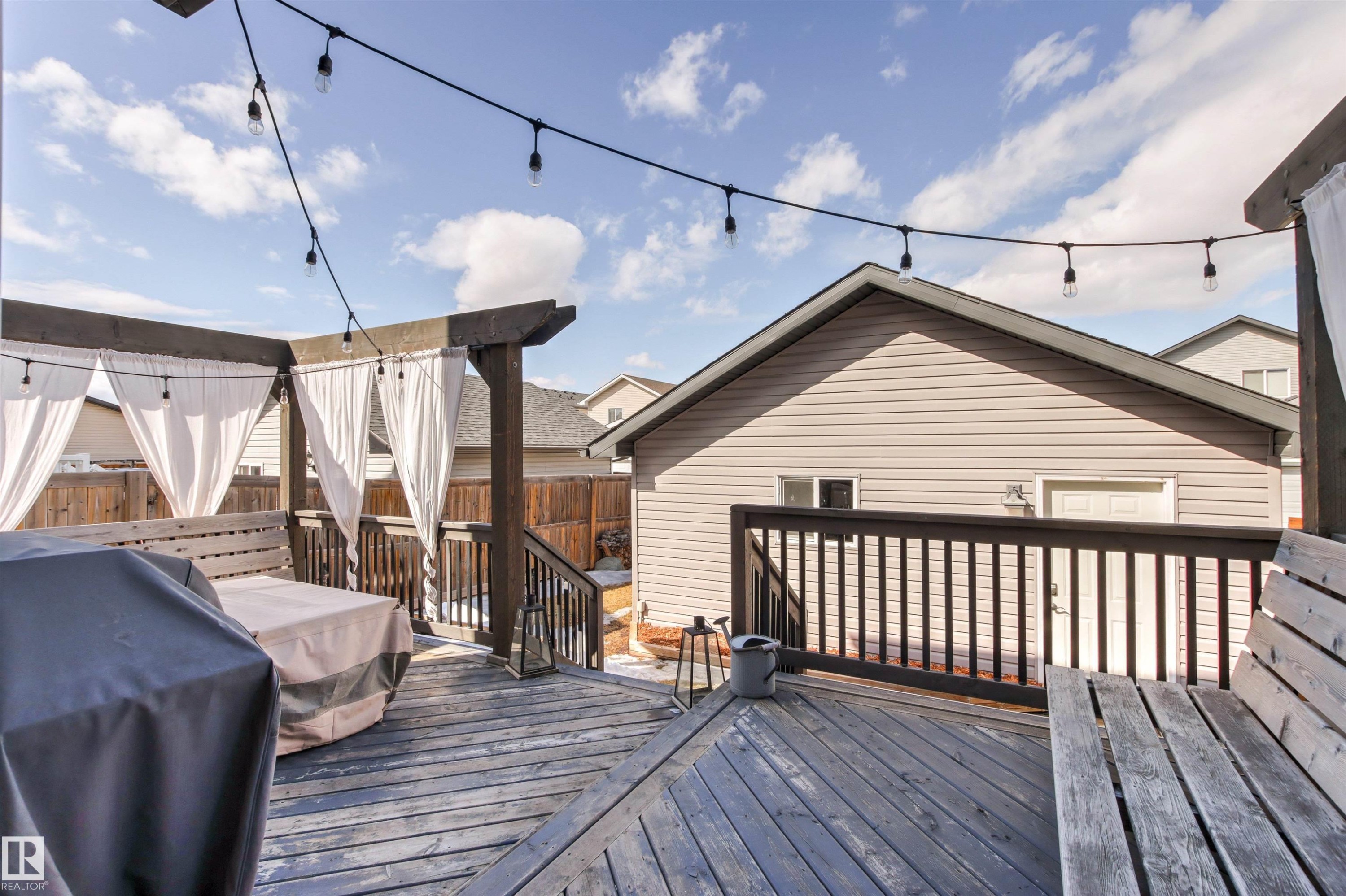 The property features a wooden deck with a pergola, adorned with string lights and white curtains - 38 Hewitt Circle, Spruce Grove, AB - Outdoor With Deck Patio Veranda With Exterior
