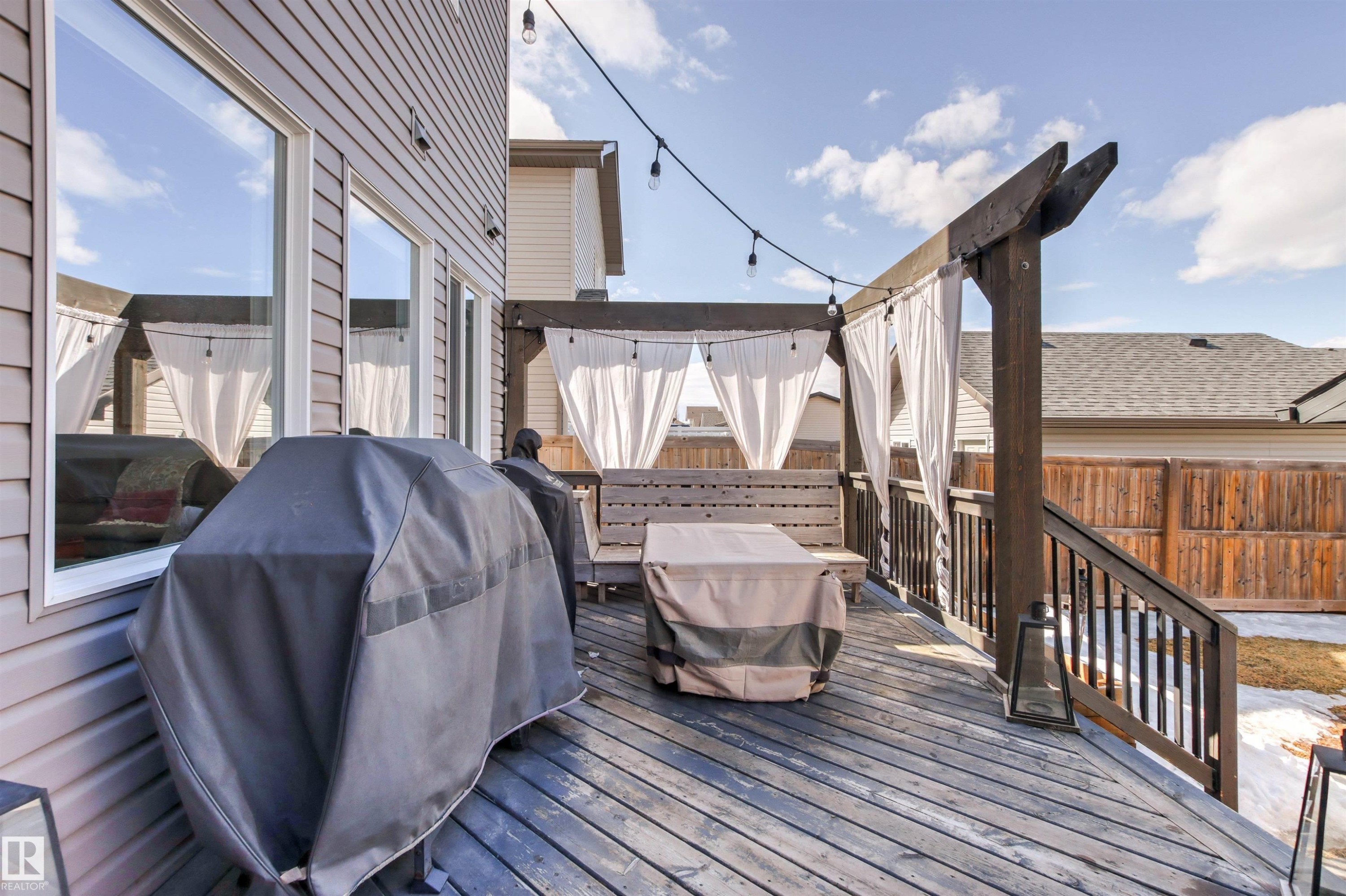 The property features an outdoor deck with wooden flooring, a wooden pergola with white fabric accents, and string lighting - 38 Hewitt Circle, Spruce Grove, AB - Outdoor With Deck Patio Veranda With Exterior