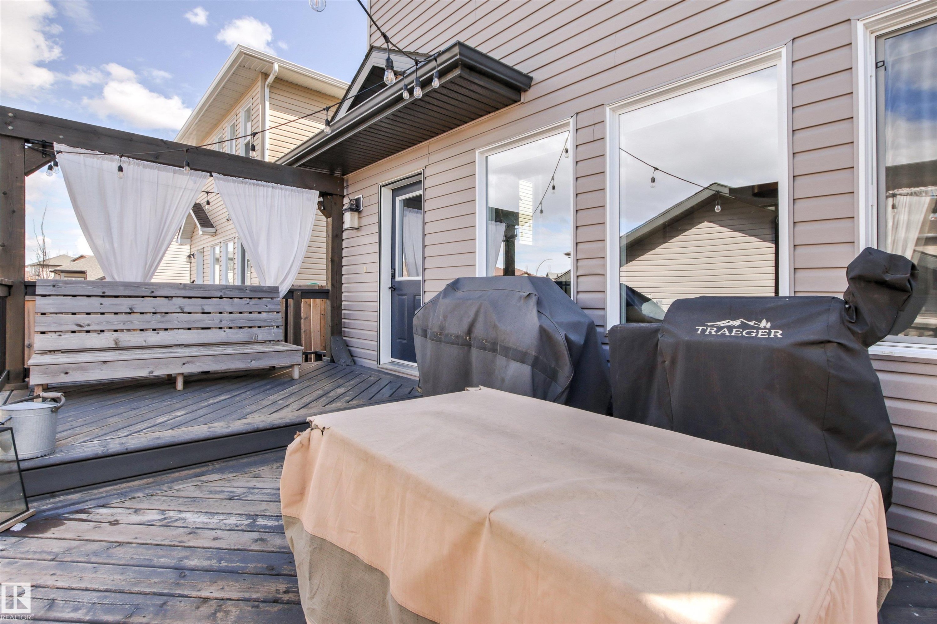The property features a wooden deck with a pergola, string lighting, and a private seating area with white privacy drapes - 38 Hewitt Circle, Spruce Grove, AB - Outdoor With Deck Patio Veranda