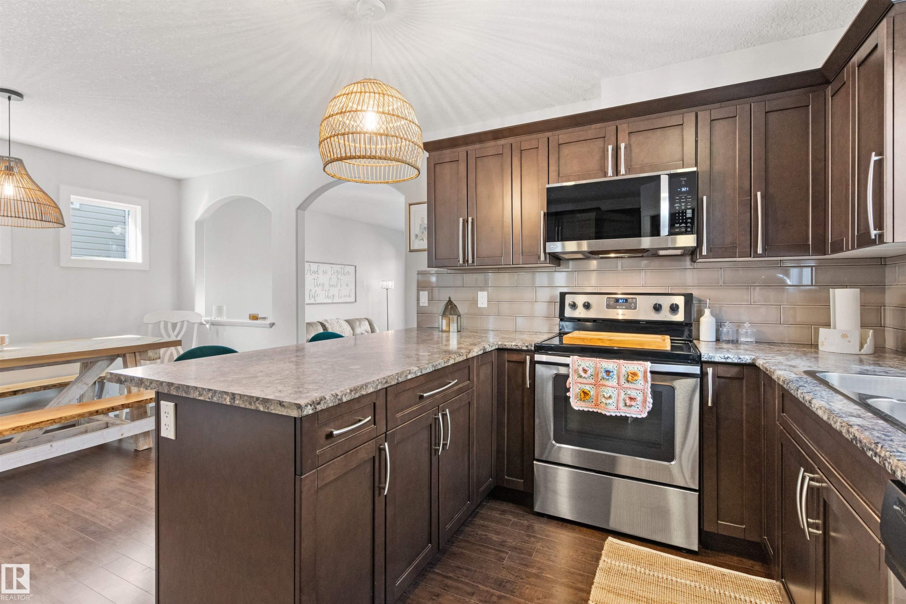 The kitchen features dark wood cabinetry, stainless steel appliances, a tile backsplash, and a spacious island with a countertop - 38 Hewitt Circle, Spruce Grove, AB - Indoor Photo Showing Kitchen With Stainless Steel Kitchen With Upgraded Kitchen