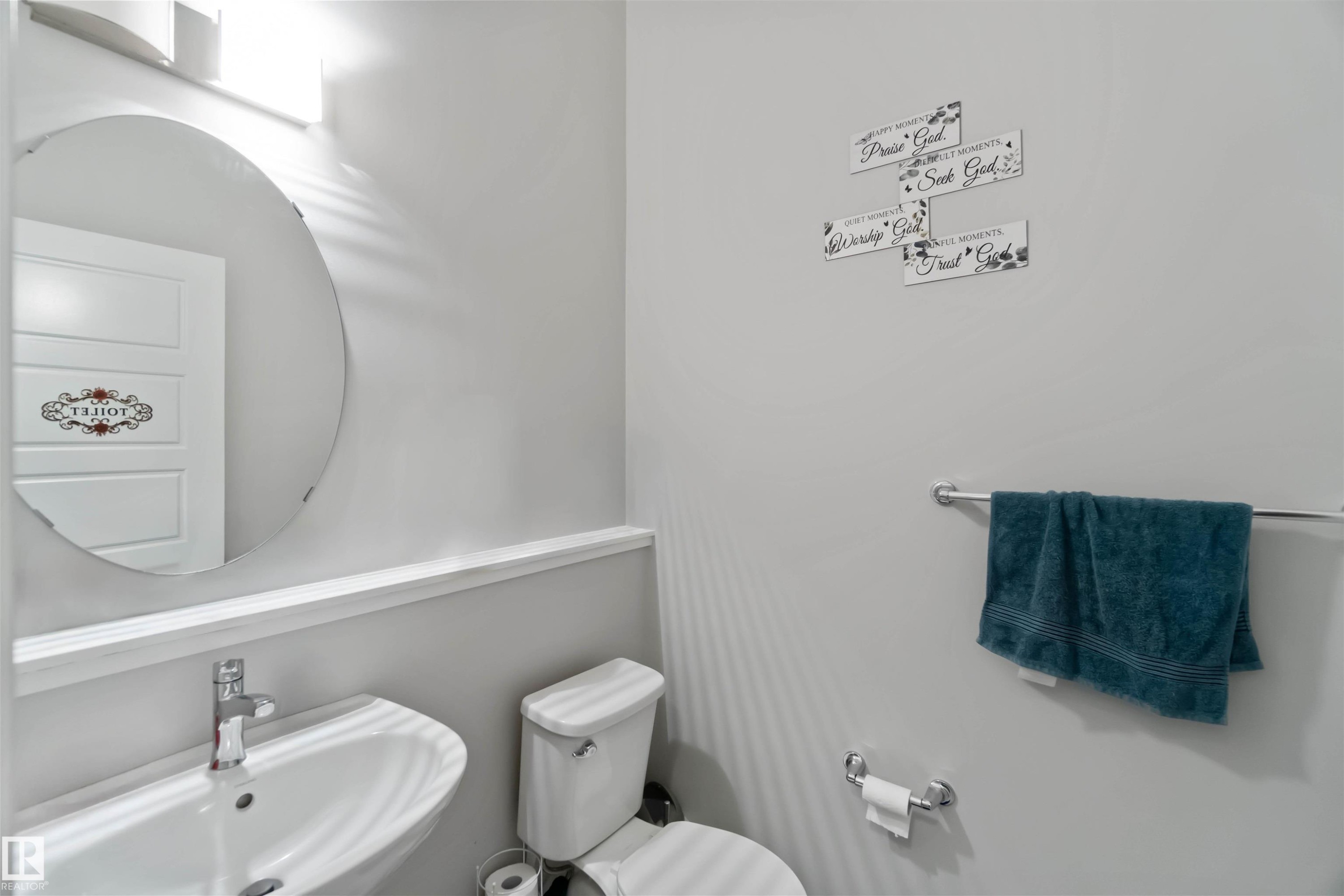 Well-appointed powder room featuring a wall-mounted sink with a modern faucet, an oval mirror, and a toilet - 2725 Orchards Road, Edmonton, AB - Indoor Photo Showing Bathroom