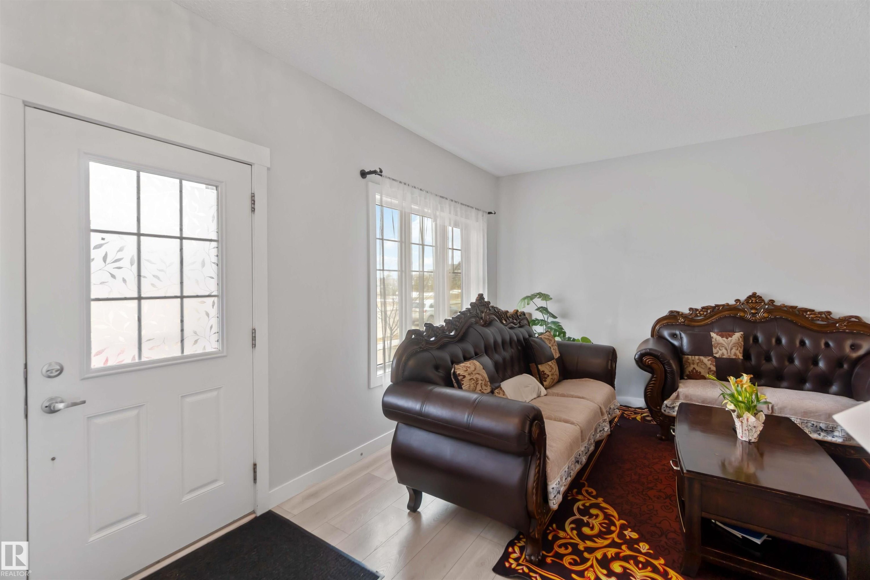 This bright and airy living space features a white entry door with decorative glass, light-toned flooring, and a window providing natural light - 2725 Orchards Road, Edmonton, AB - Indoor Photo Showing Living Room