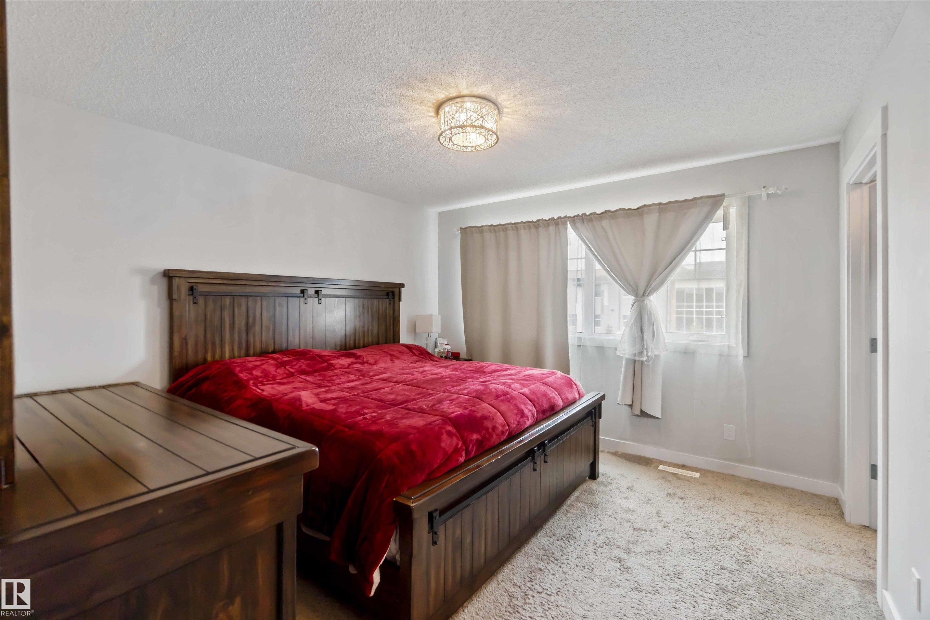 Bedroom with light-colored carpeting, white walls, and a decorative ceiling light fixture - 2725 Orchards Road, Edmonton, AB - Indoor Photo Showing Bedroom