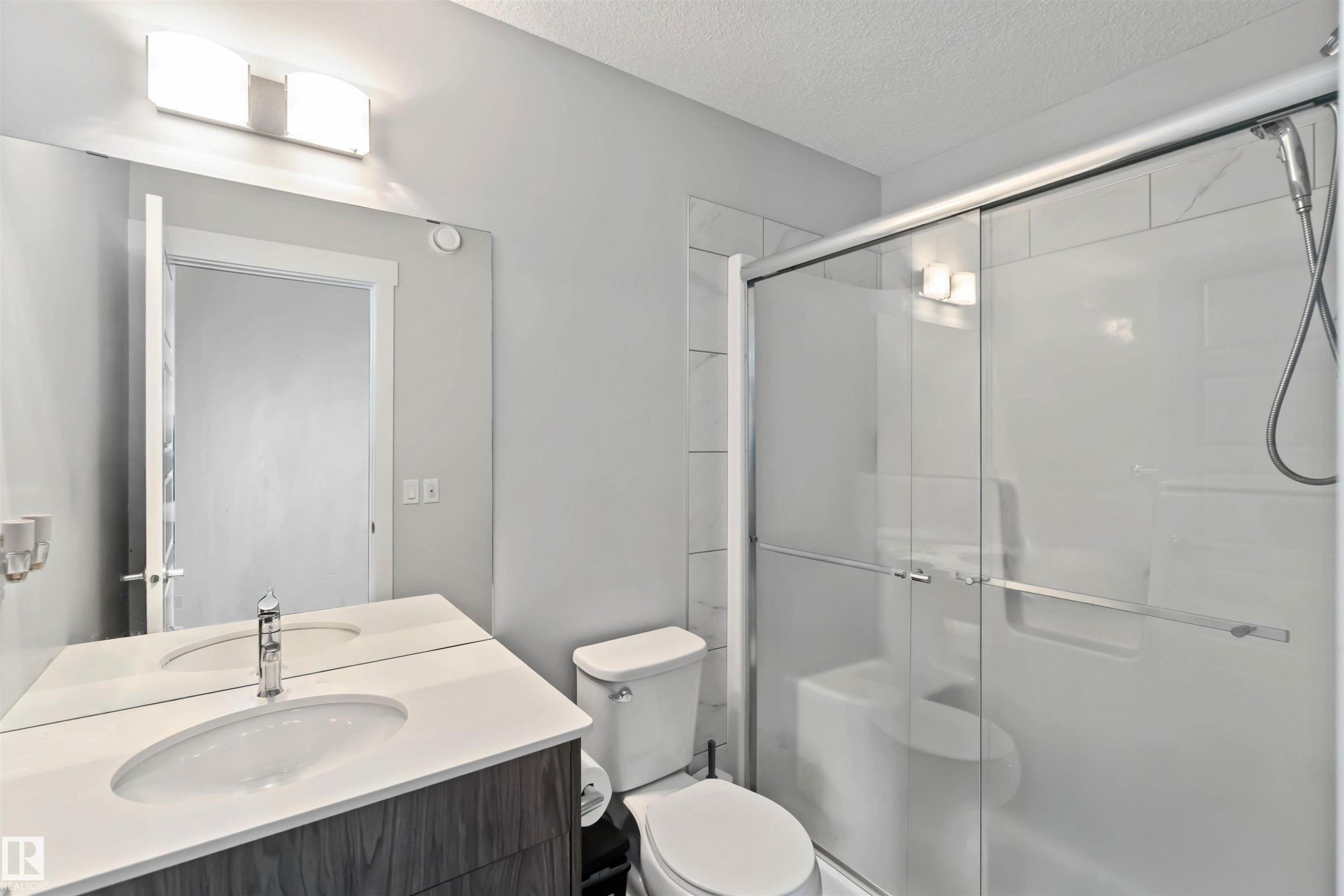Bathroom featuring a vanity with a white countertop and an integrated sink, a large mirror, a toilet, and a glass-enclosed shower with a handheld showerhead - 2725 Orchards Road, Edmonton, AB - Indoor Photo Showing Bathroom