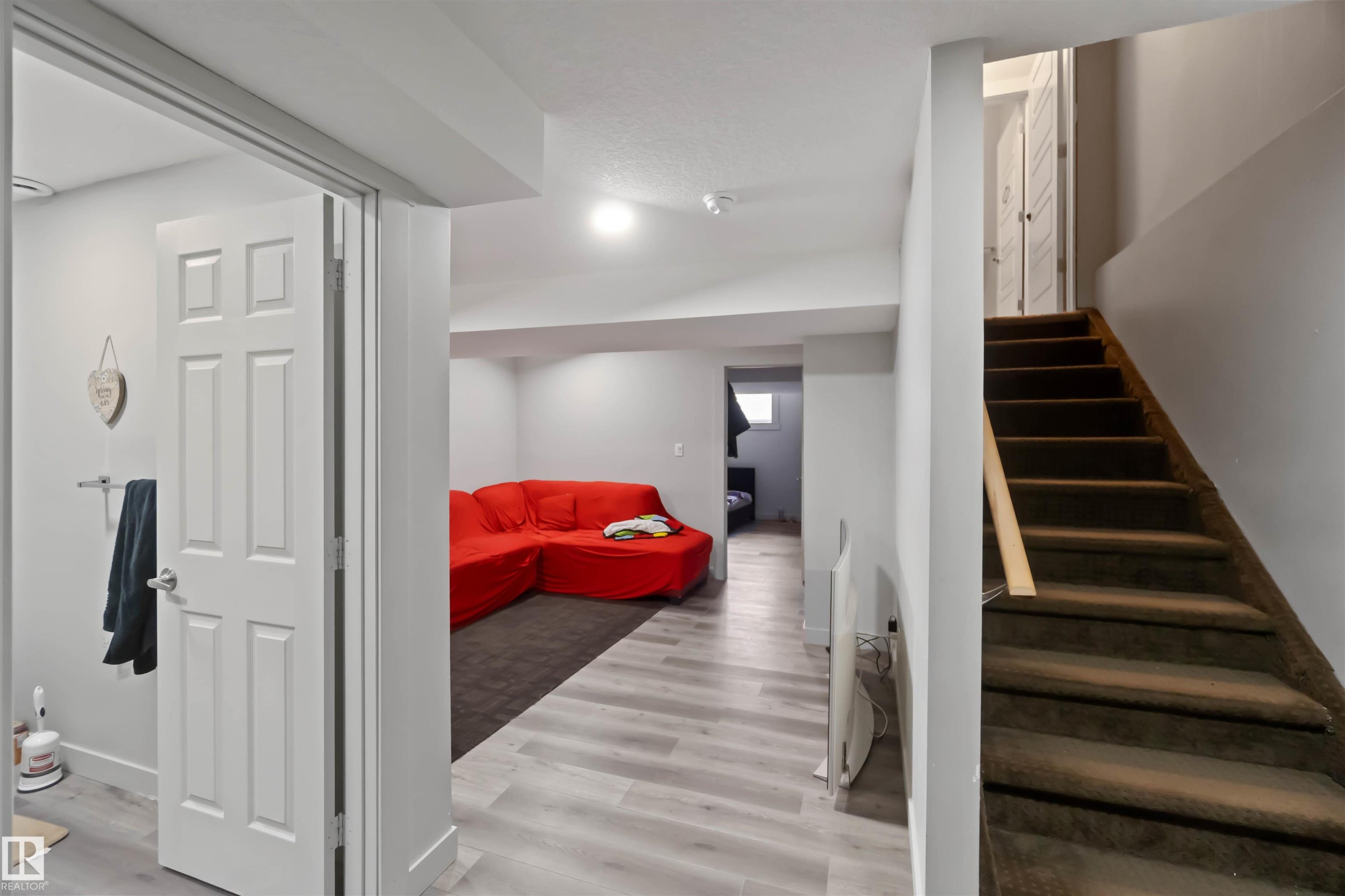 The property features a spacious room with light-toned flooring and a dark rug, along with a staircase leading upwards - 2725 Orchards Road, Edmonton, AB - Indoor Photo Showing Other Room
