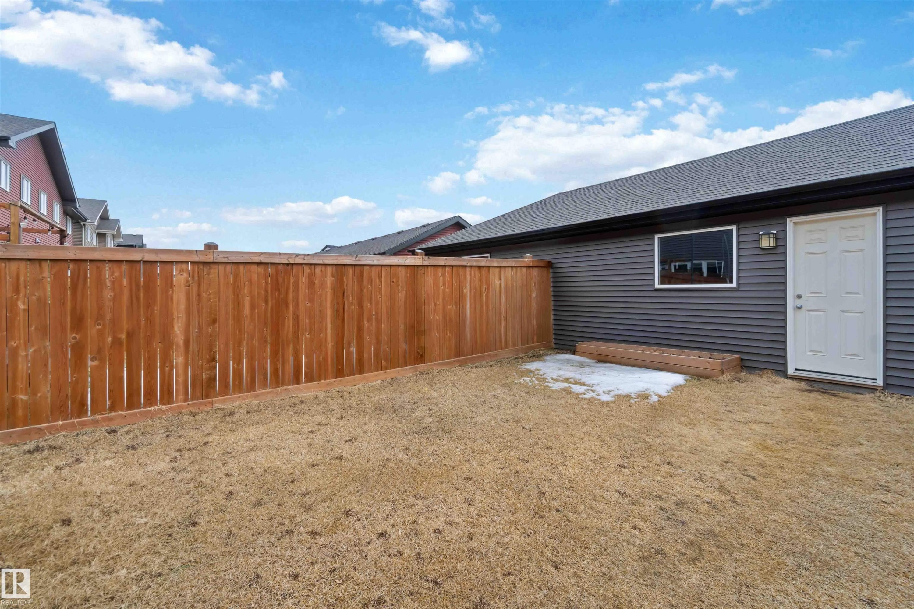 The property features a private yard with a wooden fence and a building with grey siding, a white door, and a window - 2725 Orchards Road, Edmonton, AB - Outdoor