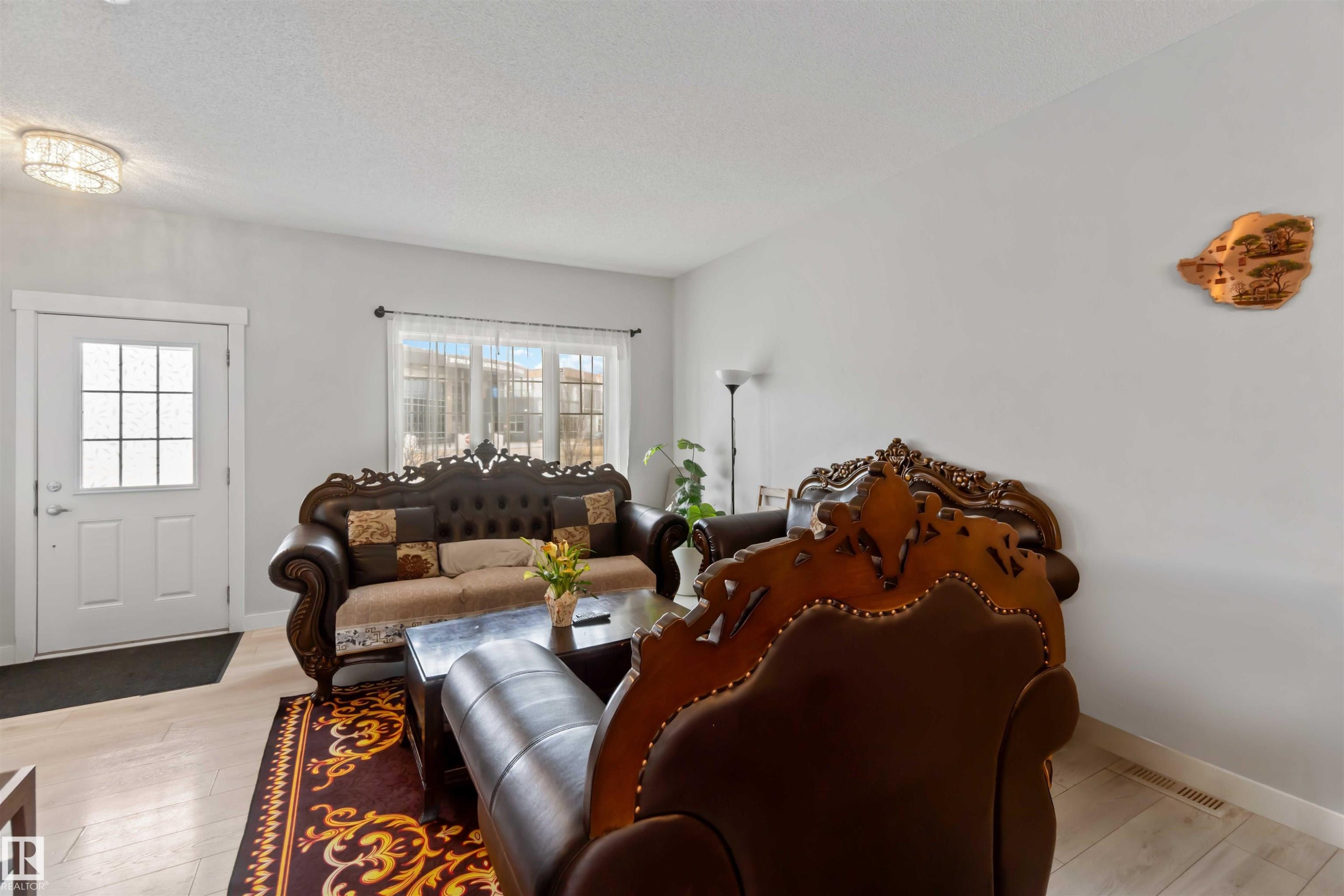 The living area features light-toned flooring, a decorative area rug, and a front entry door with glass paneling - 2725 Orchards Road, Edmonton, AB - Indoor Photo Showing Living Room