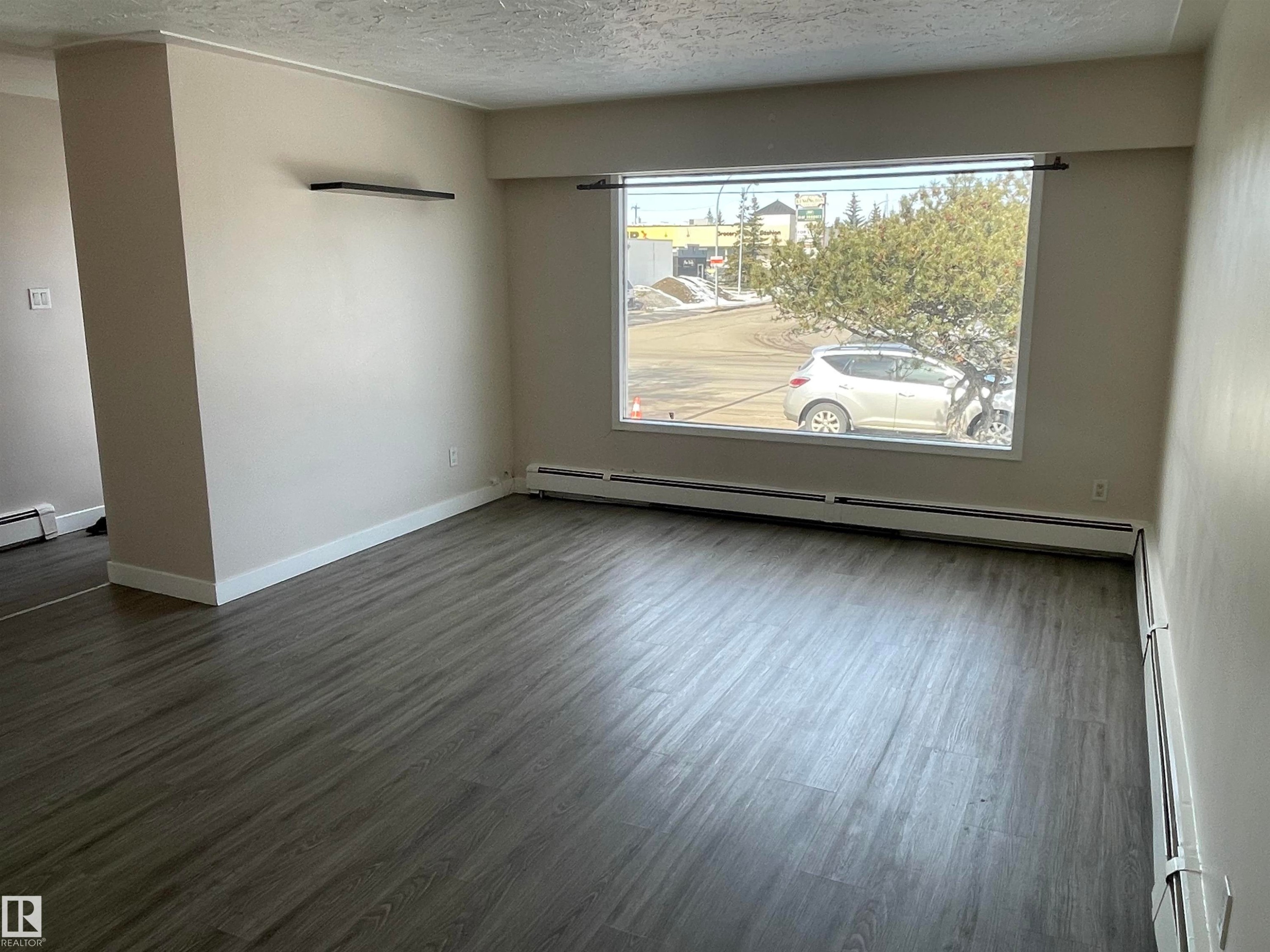 The living area features durable wood-look flooring and a large window providing views of the surrounding outdoor area - 12335 132 Avenue, Edmonton, AB - Indoor Photo Showing Other Room