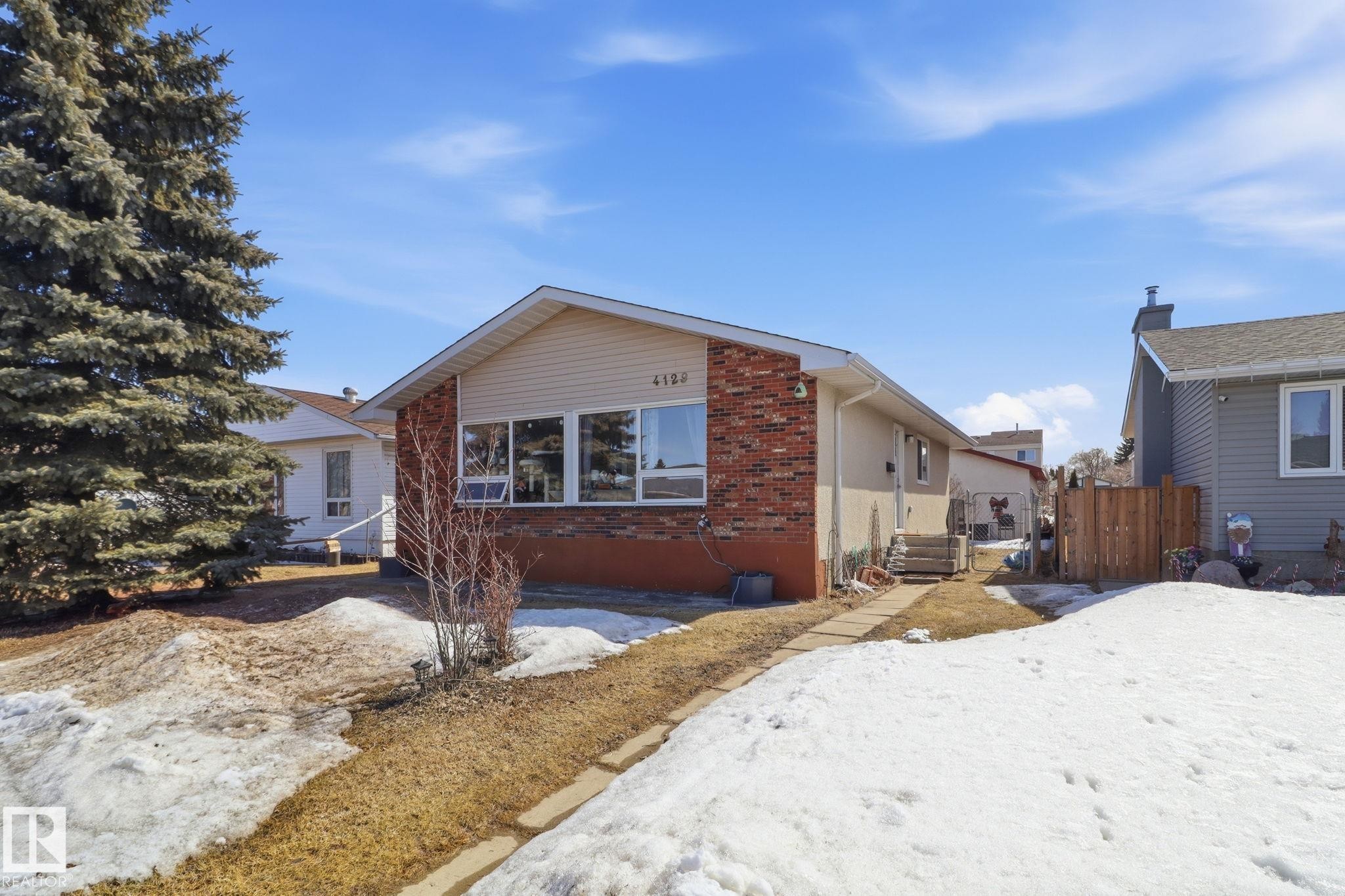 The property features a brick and siding exterior, a front walkway, and a large evergreen tree - 4129 134A Avenue Nw, Edmonton, AB - Outdoor