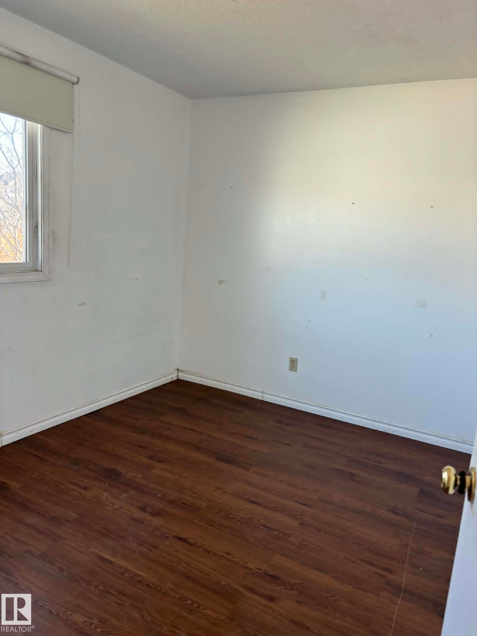 Room featuring wood-finish flooring, white baseboards, a white wall finish, and a window with a roller shade - 4129 134A Avenue Nw, Edmonton, AB - Indoor Photo Showing Other Room