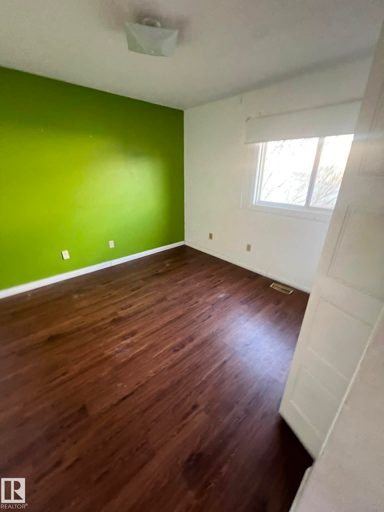 Room featuring wood-finish flooring, a prominent accent wall, and a ceiling-mounted light fixture - 4129 134A Avenue Nw, Edmonton, AB - Indoor Photo Showing Other Room