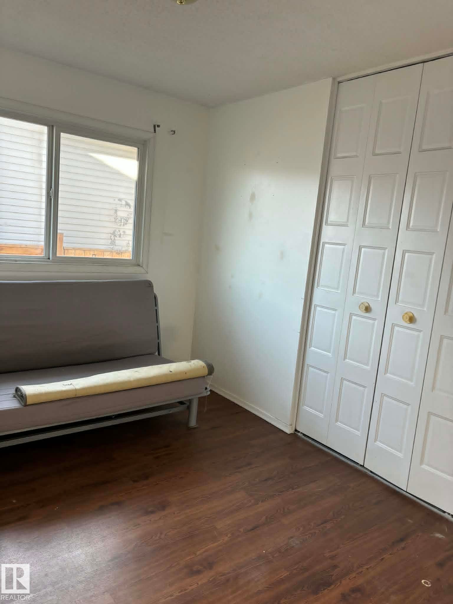 Room featuring wood-finish flooring, a double window with blinds, and white bi-fold closet doors with round brass hardware - 4129 134A Avenue Nw, Edmonton, AB - Indoor