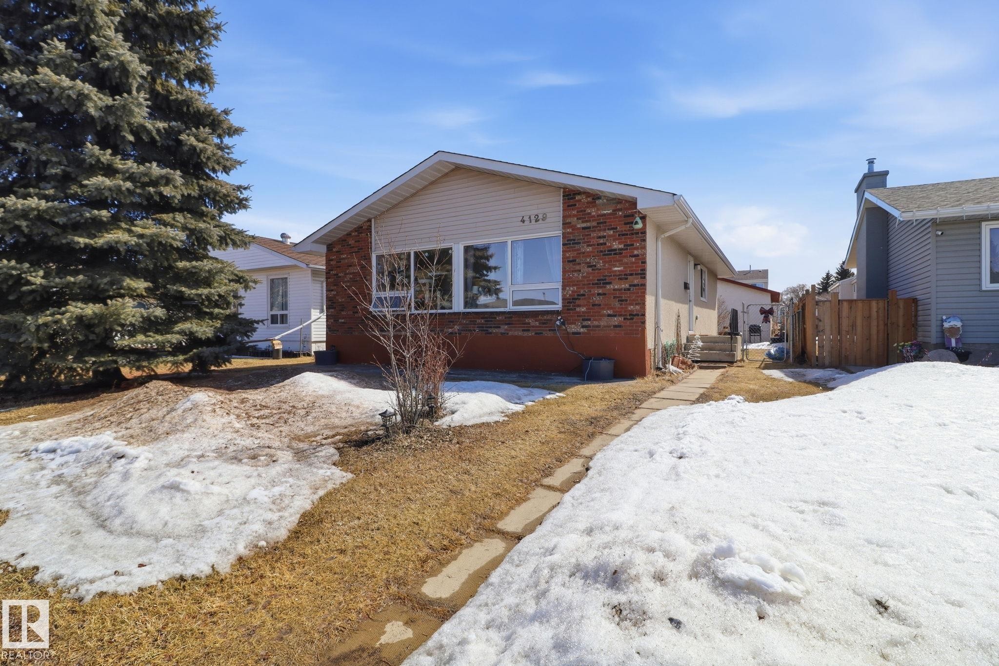 The property features a brick and siding exterior, with a large evergreen tree in the front yard - 4129 134A Avenue Nw, Edmonton, AB - Outdoor