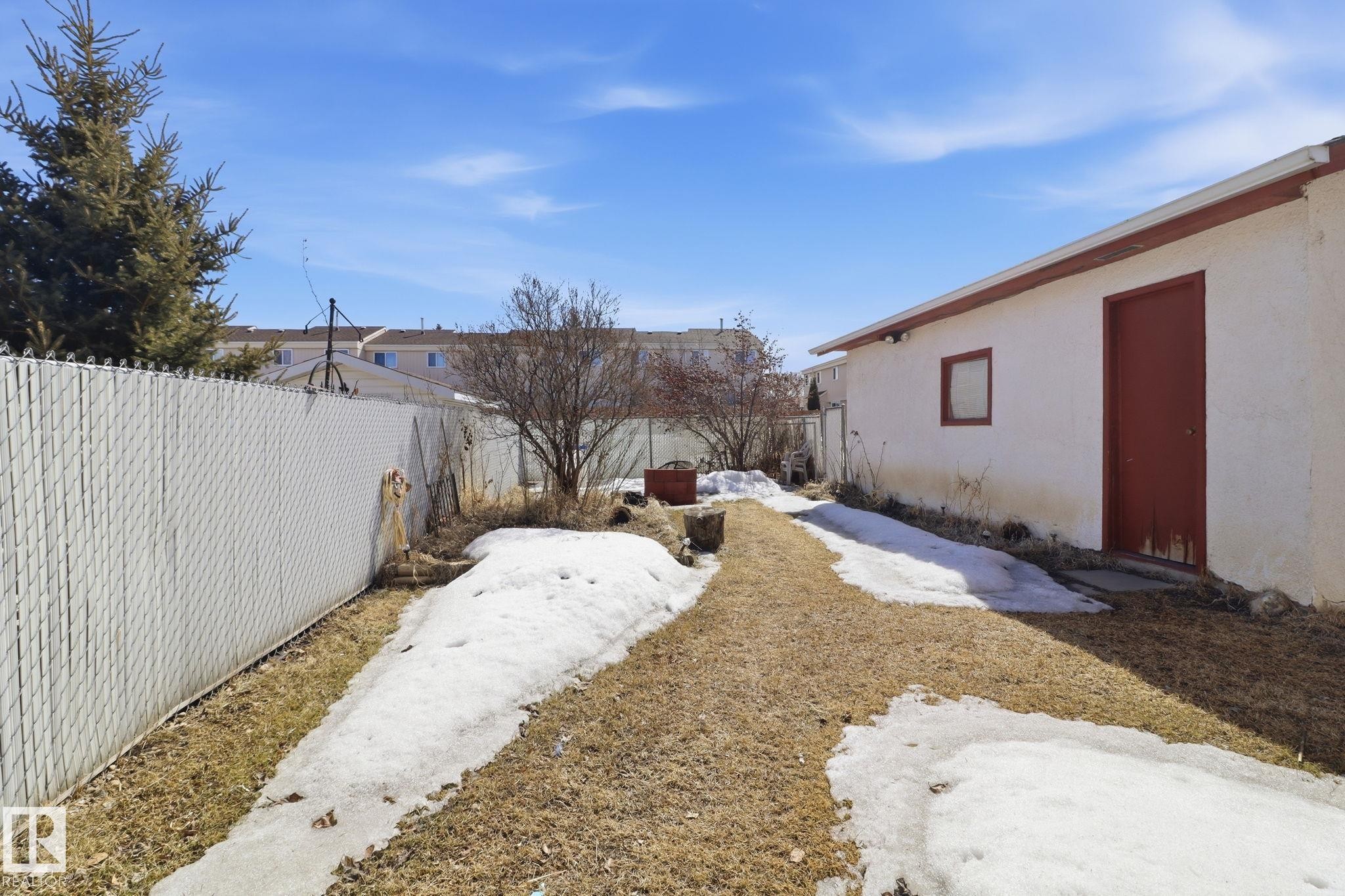 The property features an exterior building with a red door and a small window, set within a yard that includes a pathway, patches of grass, and areas of snow - 4129 134A Avenue Nw, Edmonton, AB - Outdoor