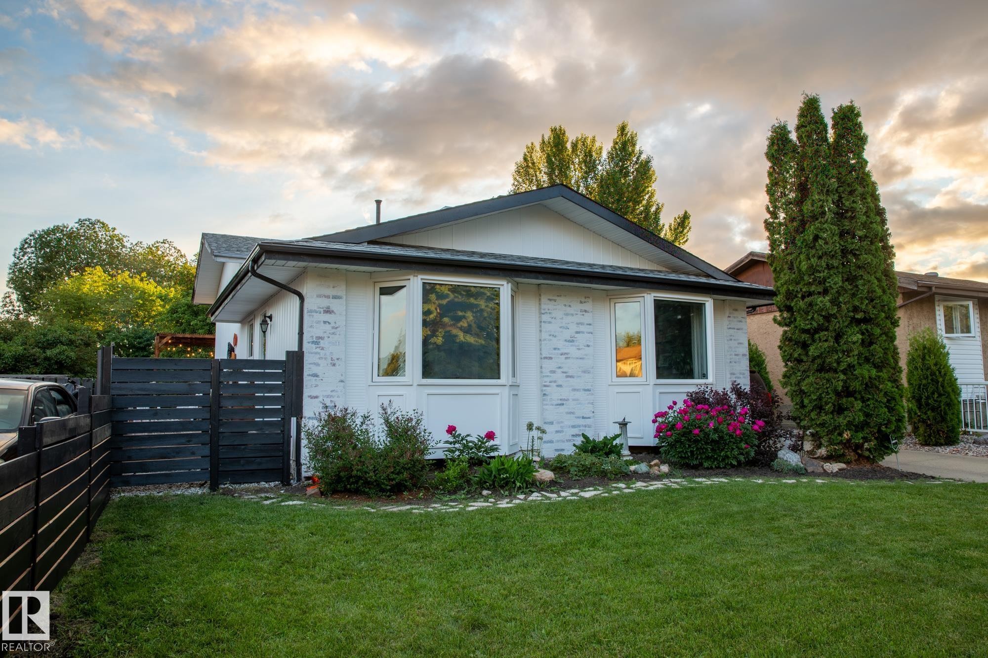 The property features a well-maintained lawn, established landscaping with flowering bushes, and mature trees - 2626 49 Street, Edmonton, AB - Outdoor