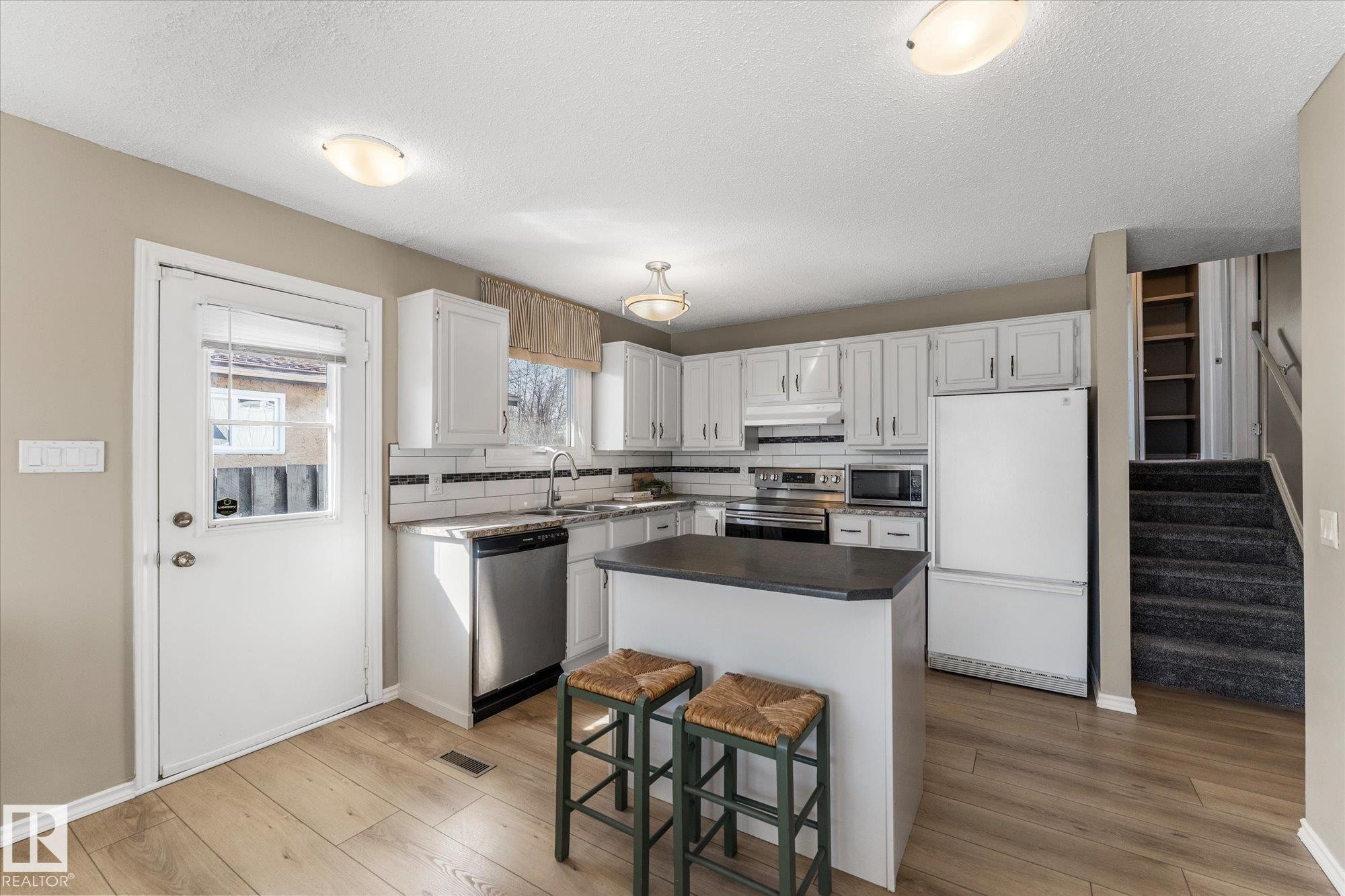 The kitchen features light-toned flooring, white cabinetry, a kitchen island with seating, and stainless steel appliances - 2626 49 Street, Edmonton, AB - Indoor Photo Showing Kitchen
