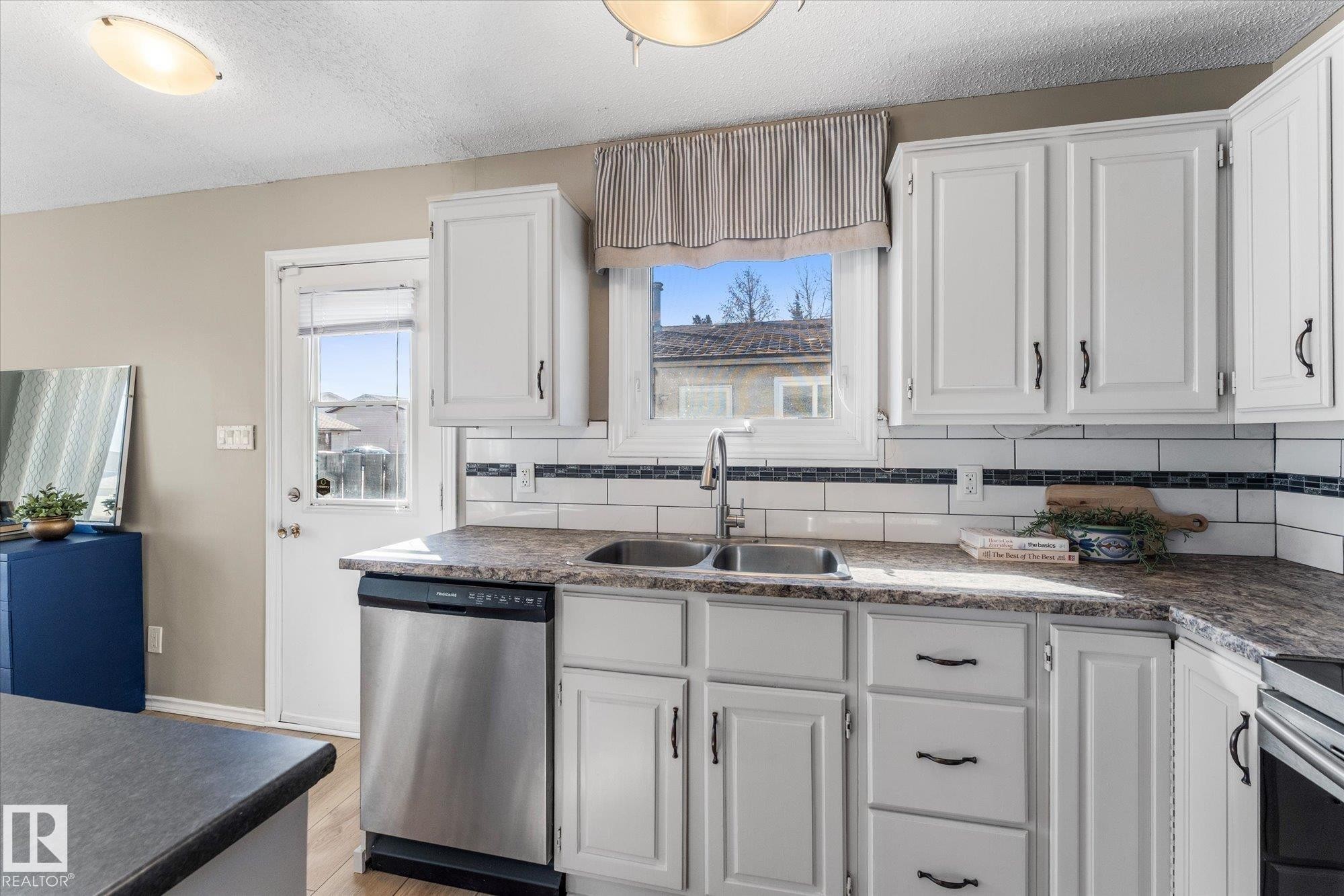 The kitchen features white cabinetry, a double basin sink, and stainless steel appliances, including a dishwasher - 2626 49 Street, Edmonton, AB - Indoor Photo Showing Kitchen With Double Sink