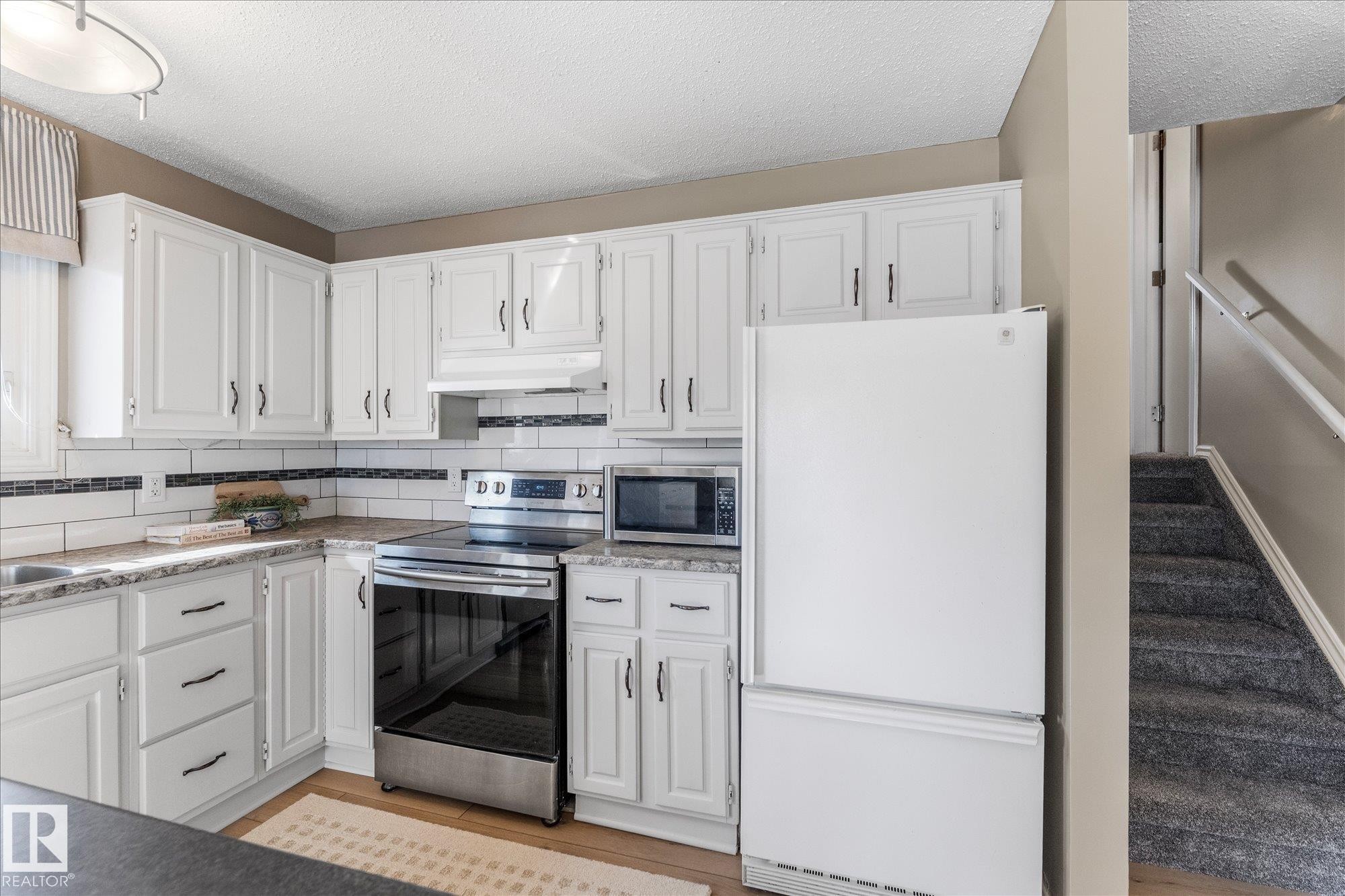 The kitchen features white cabinetry, a white subway tile backsplash with dark accents, and a stainless steel oven and range - 2626 49 Street, Edmonton, AB - Indoor Photo Showing Kitchen