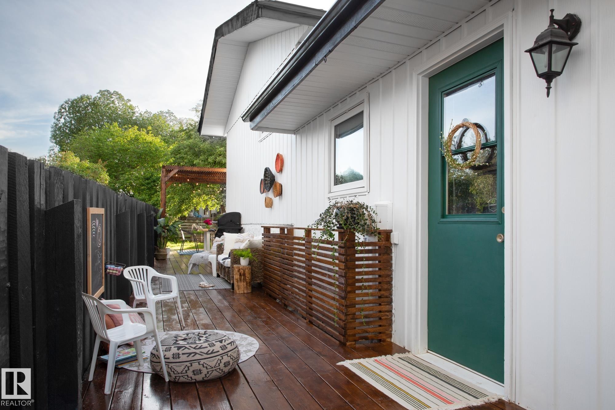The property features a dark wooden deck with a white exterior, a green entry door with a window, and a black fence - 2626 49 Street, Edmonton, AB - Outdoor With Deck Patio Veranda With Exterior