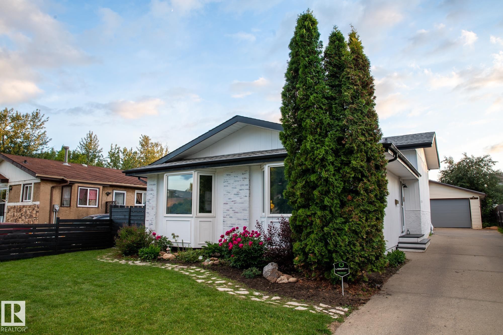 The property features a well-maintained lawn, a paved driveway, and established landscaping with mature trees and flowering shrubs - 2626 49 Street, Edmonton, AB - Outdoor