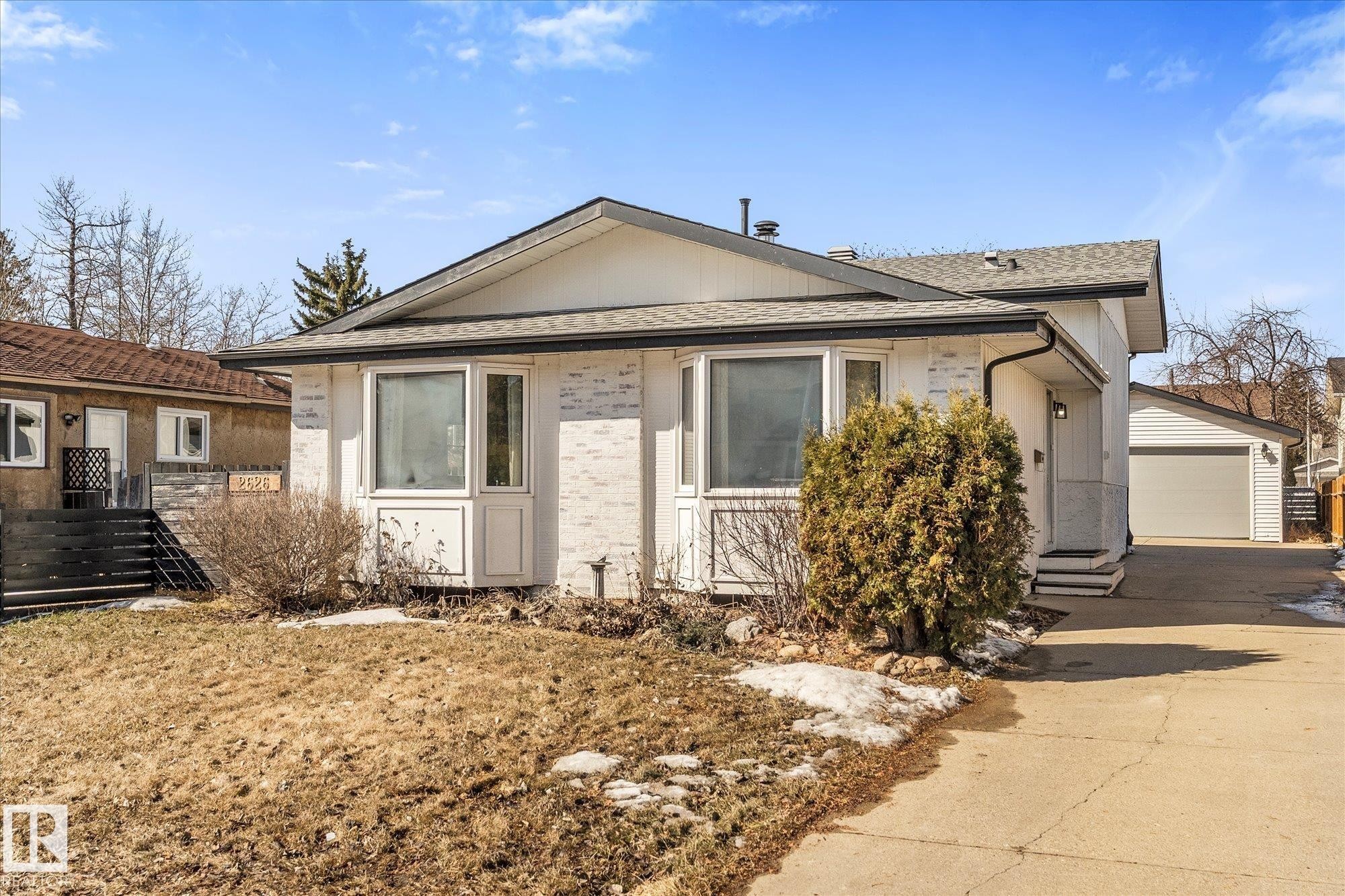 The property features a white exterior with brick accents, a dark asphalt shingle roof, and a paved driveway leading to a single garage - 2626 49 Street, Edmonton, AB - Outdoor