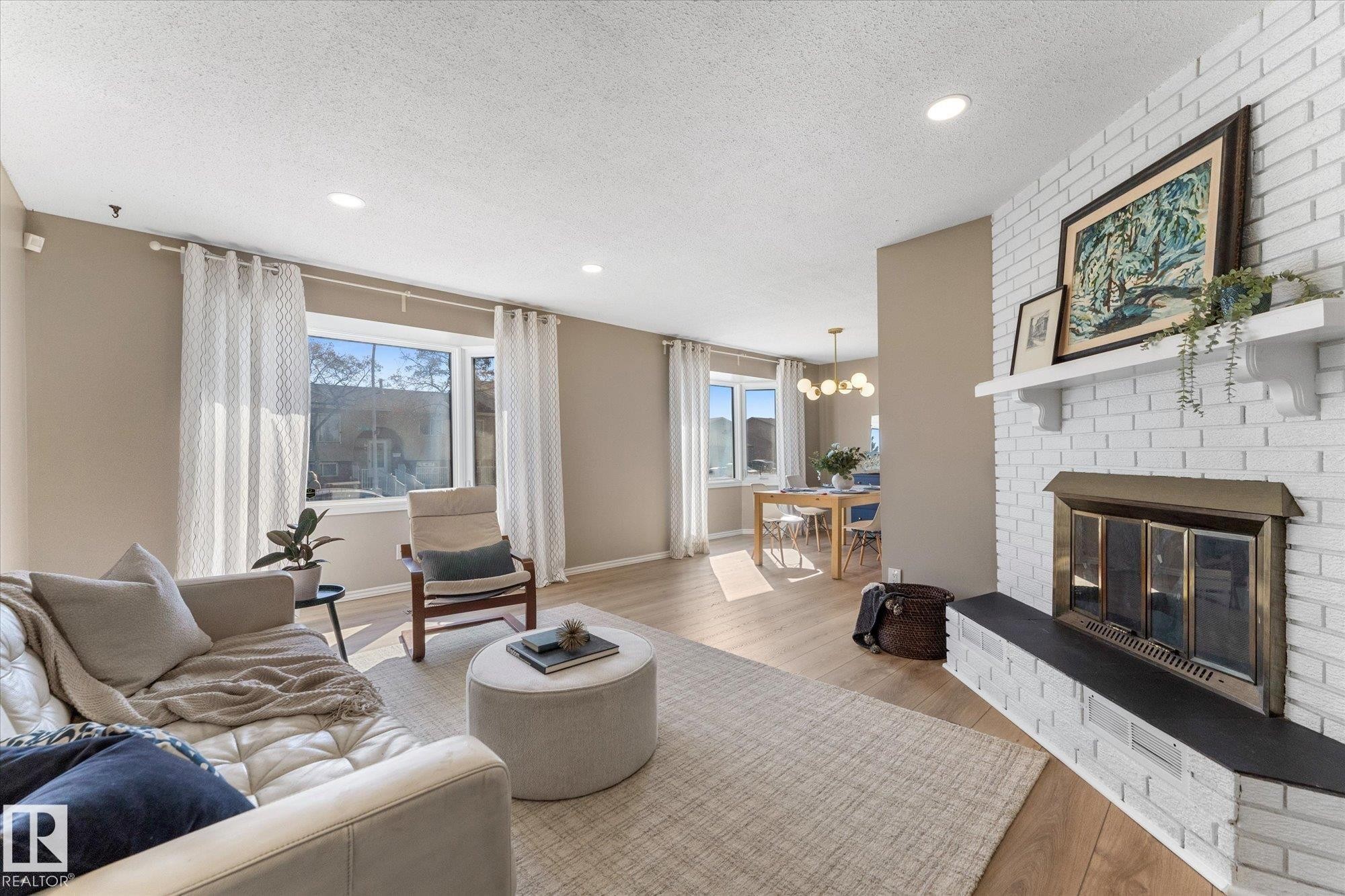 The living area features a white brick fireplace with a black hearth, recessed lighting, and light-colored flooring - 2626 49 Street, Edmonton, AB - Indoor Photo Showing Living Room With Fireplace