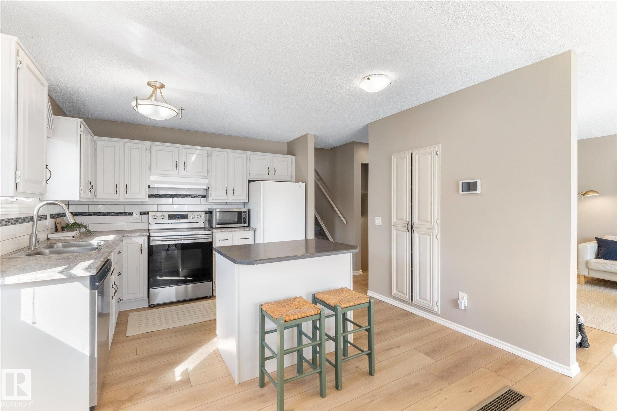 The kitchen features white cabinetry, stainless steel appliances, a white tile backsplash, and an island with a dark countertop - 2626 49 Street, Edmonton, AB - Indoor Photo Showing Kitchen