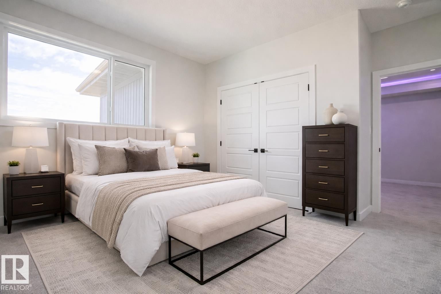 This bedroom features a large window providing ample natural light, a neutral color palette, and light-colored carpeting - Rural Leduc County, AB - Indoor Photo Showing Bedroom