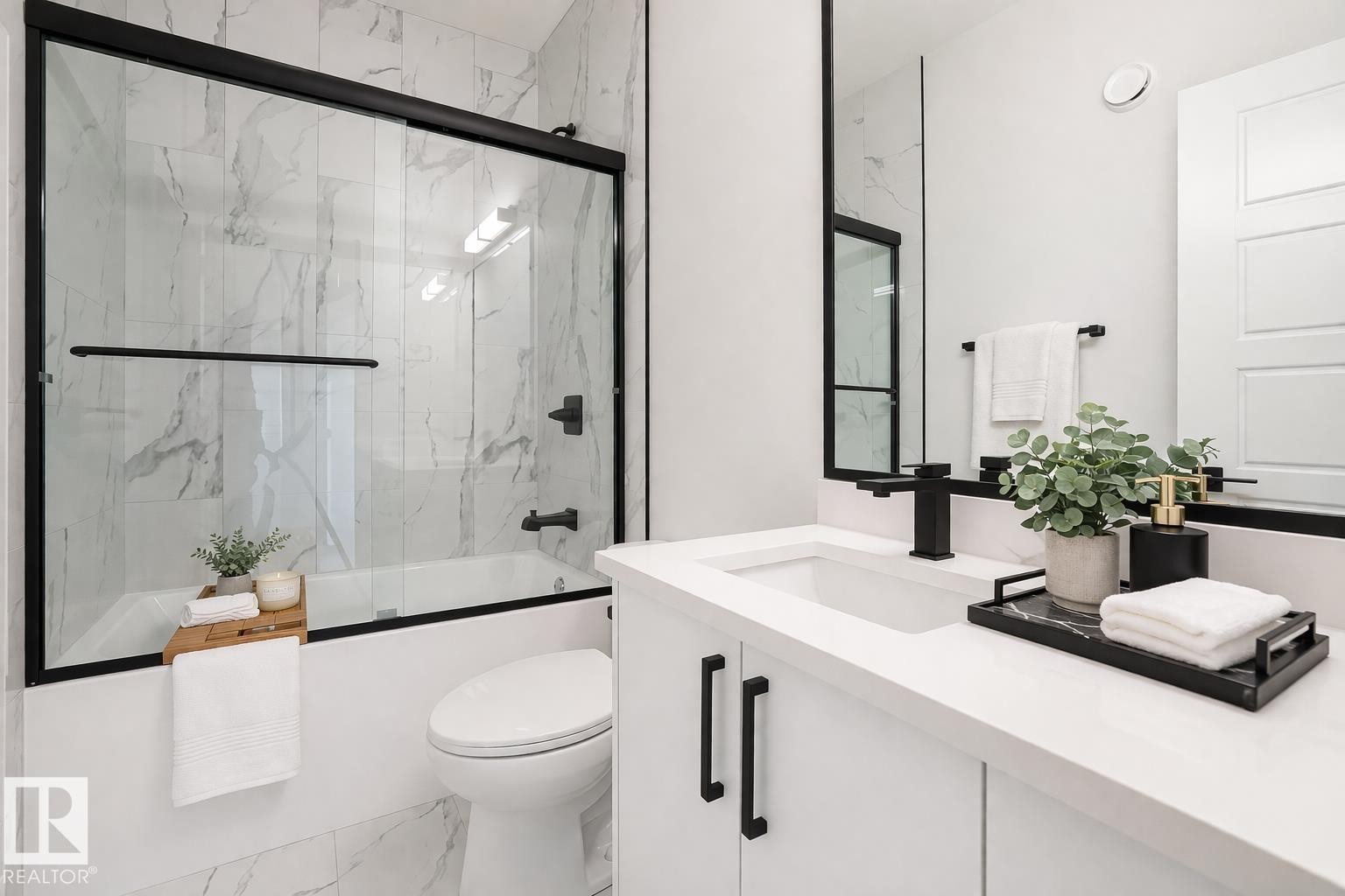 Bathroom featuring a modern vanity with a white countertop and black fixtures, a white bathtub with a glass enclosure, and white marble-style wall and floor tiling - Rural Leduc County, AB - Indoor Photo Showing Bathroom