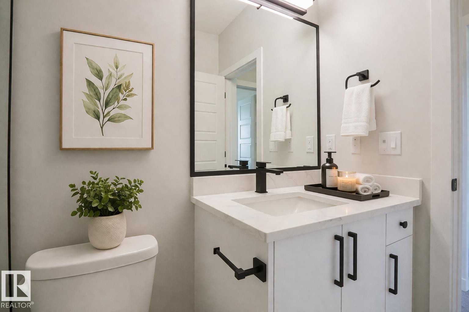 Bathroom featuring a vanity with a white countertop and white cabinetry, a rectangular mirror with a black frame, and a white toilet - Rural Leduc County, AB - Indoor Photo Showing Bathroom