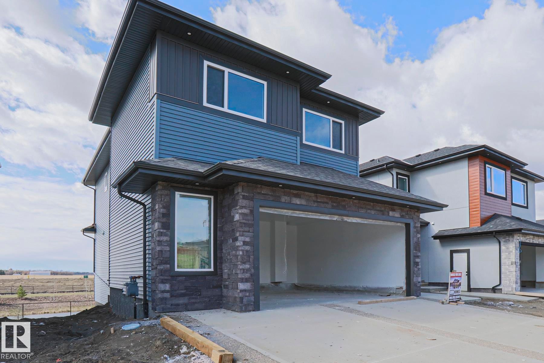 The property features a modern exterior with blue and dark grey siding, stone accents, and an integrated garage - Rural Leduc County, AB - Outdoor