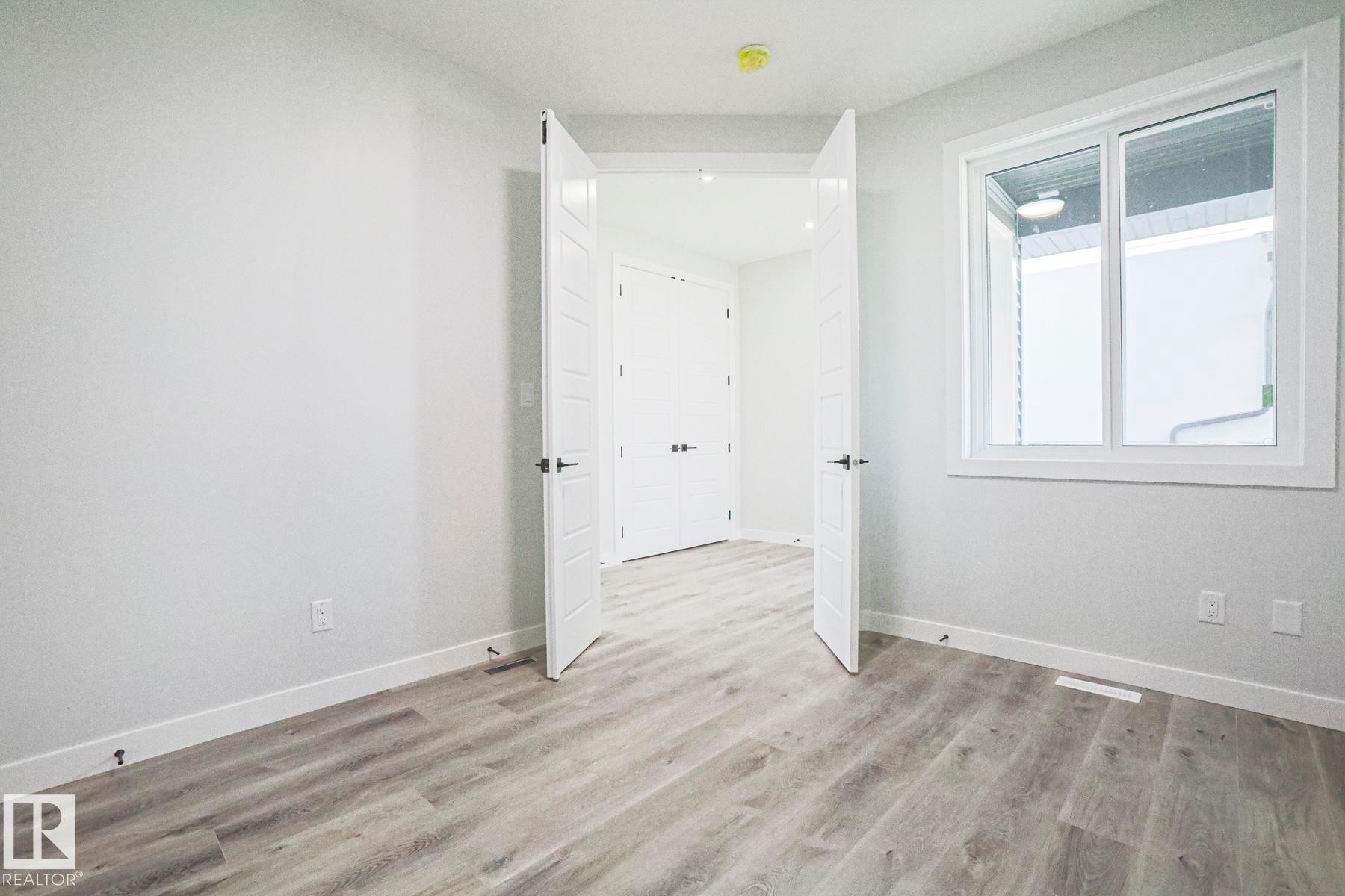 The property features light-colored laminate flooring and a white window with a view of an exterior wall - Rural Leduc County, AB - Indoor Photo Showing Other Room