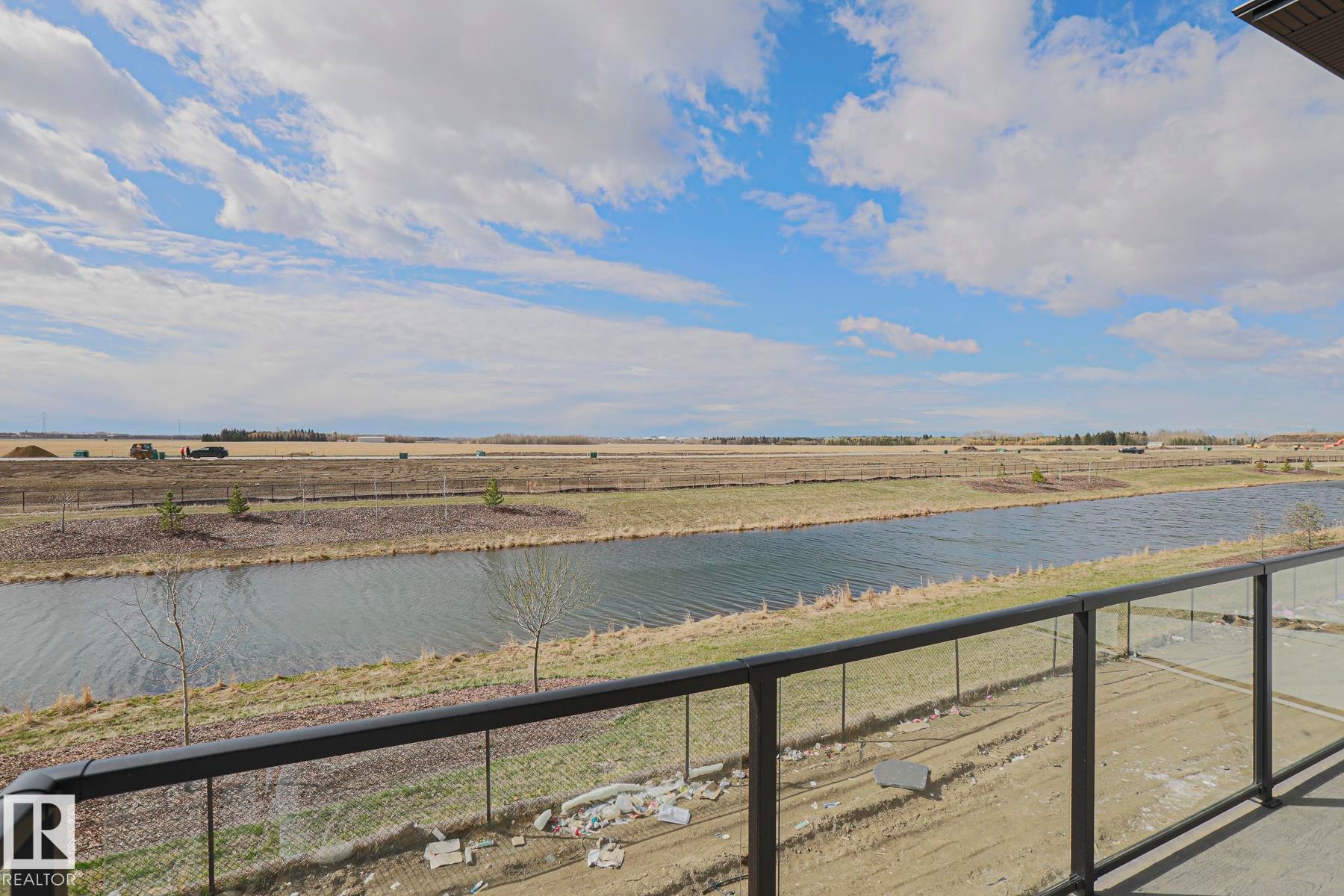 Outdoor balcony with a glass railing provides an expansive view of the surrounding landscape, including a body of water and open fields - Rural Leduc County, AB - Outdoor With Body Of Water With View