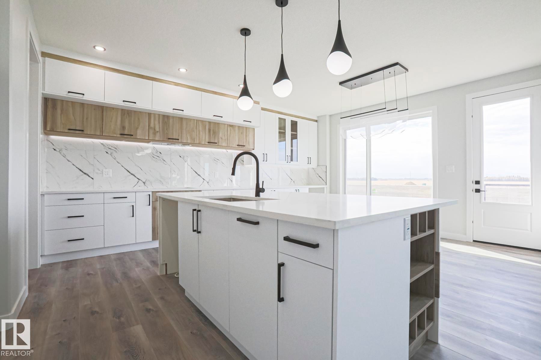 The kitchen features modern white cabinetry, a large island with a countertop, and a white marble-patterned backsplash - Rural Leduc County, AB - Indoor Photo Showing Kitchen With Upgraded Kitchen