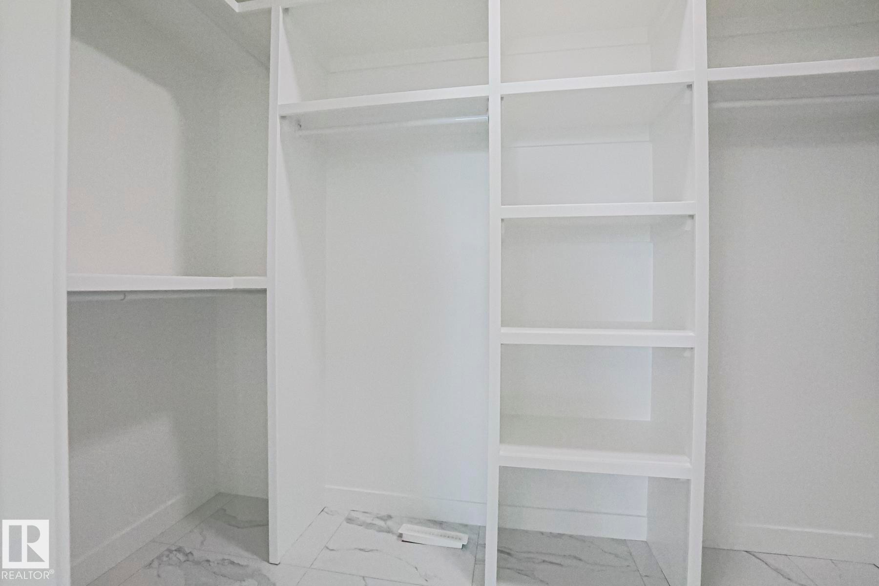 The property features a closet with built-in shelving, hanging rods, and a light-colored tiled floor - Rural Leduc County, AB - Indoor With Storage