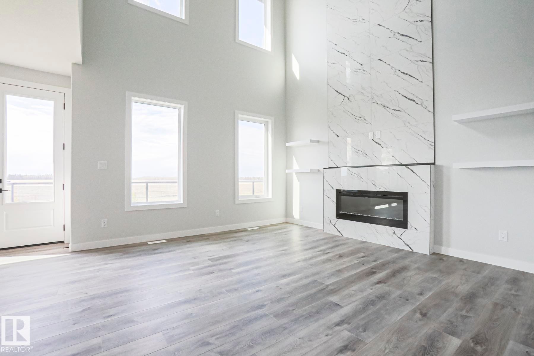 The main living area features high ceilings, wide plank flooring, and a contemporary fireplace with a large format marble surround - Rural Leduc County, AB - Indoor With Fireplace