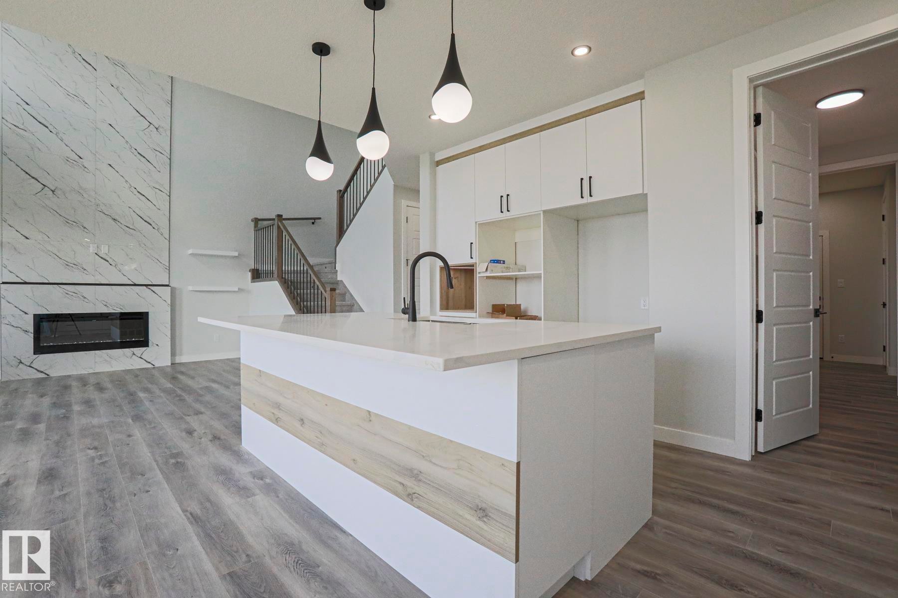 Open concept living space featuring a kitchen island with a white countertop and a black faucet, white cabinetry, and recessed lighting - Rural Leduc County, AB - Indoor With Fireplace