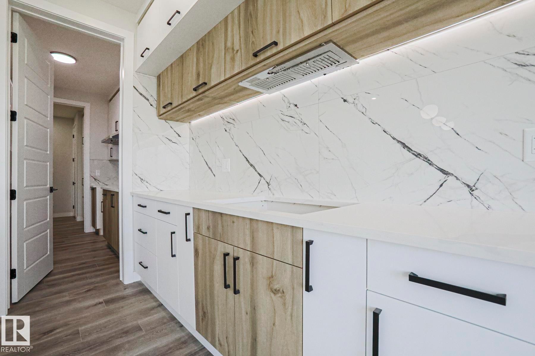 The kitchen features wood-toned and white cabinetry with black hardware, white countertops, and a white marble-patterned backsplash - Rural Leduc County, AB - Indoor Photo Showing Other Room