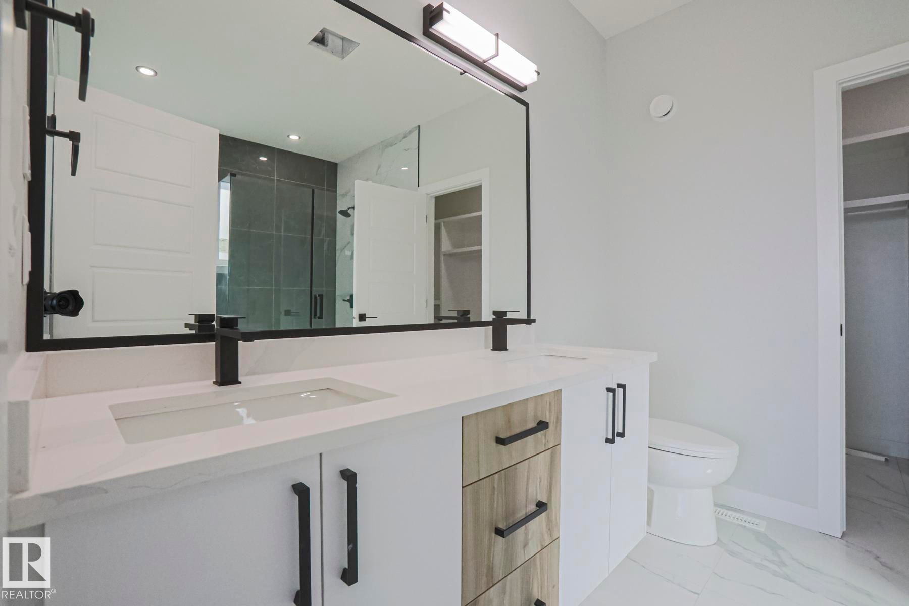 The bathroom features a double vanity with white countertops, a large mirror with a black frame, and black faucets - Rural Leduc County, AB - Indoor Photo Showing Bathroom