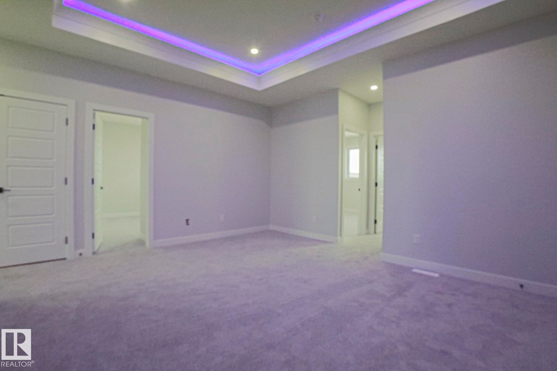 This spacious room features light-colored carpeting, white walls, and a tray ceiling with recessed lighting and accent lighting - Rural Leduc County, AB - Indoor Photo Showing Other Room