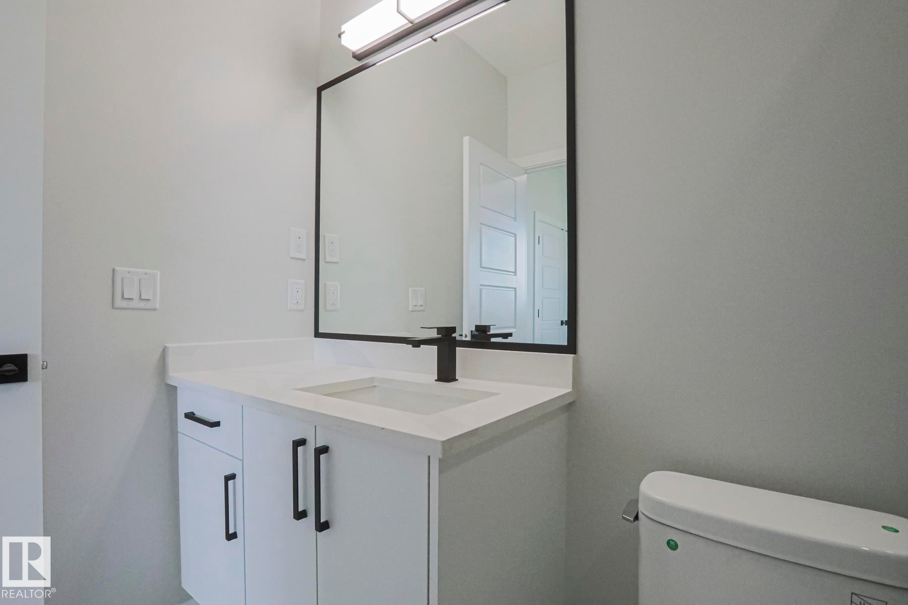 Bathroom vanity with a white countertop, an integrated sink, and a black faucet - Rural Leduc County, AB - Indoor Photo Showing Bathroom