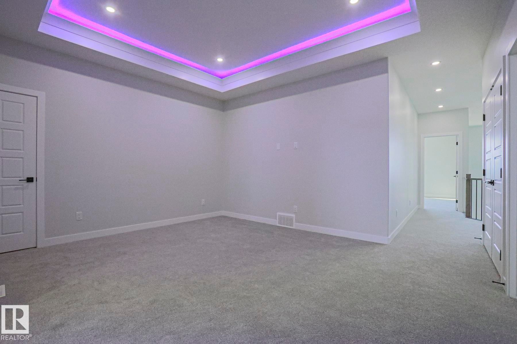 This room features plush carpet flooring and a tray ceiling with recessed lighting and accent lighting - Rural Leduc County, AB - Indoor Photo Showing Other Room