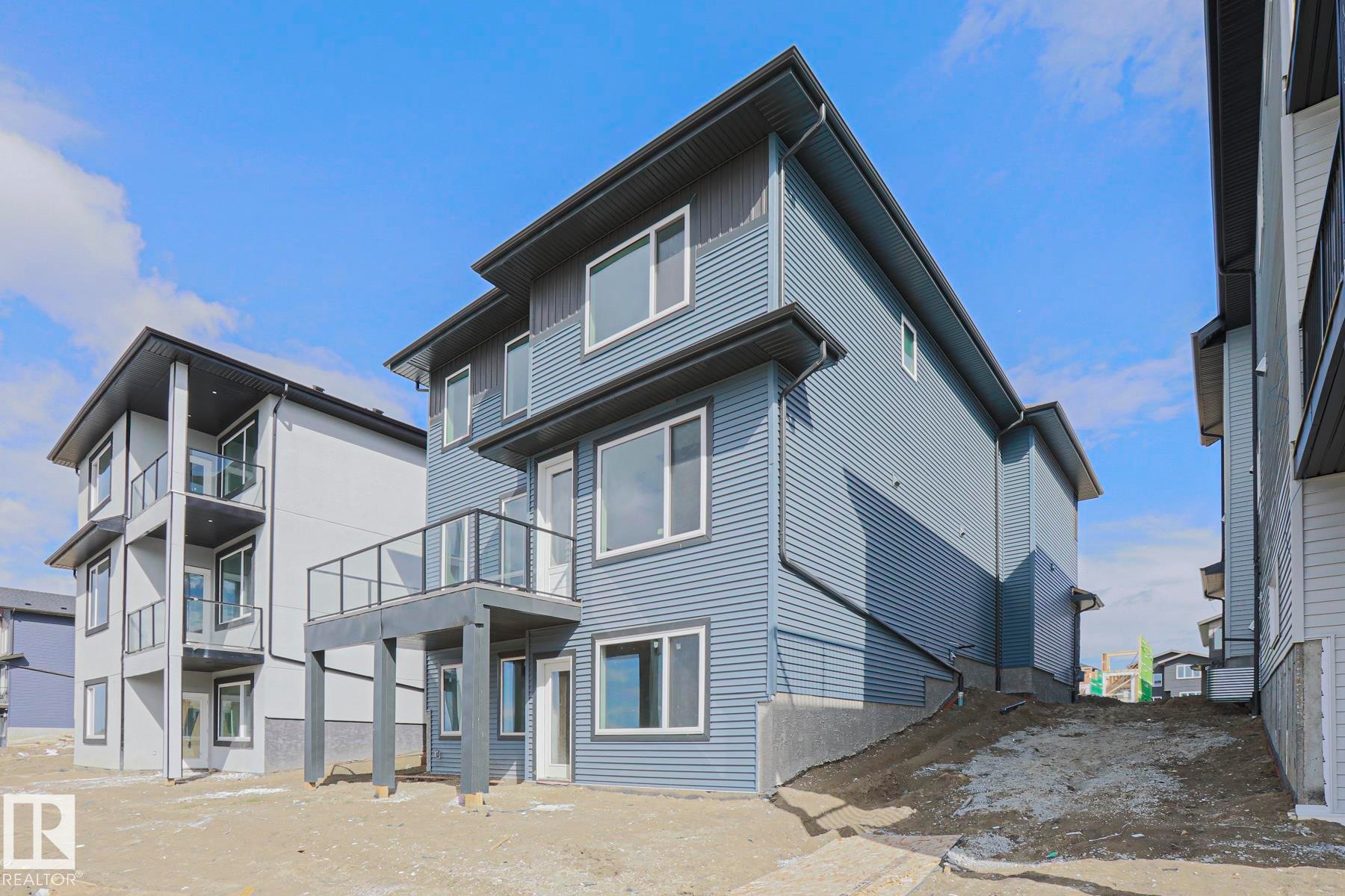 The property features contemporary architecture with blue horizontal siding, white window trim, and a second-story deck with glass railings - Rural Leduc County, AB - Outdoor